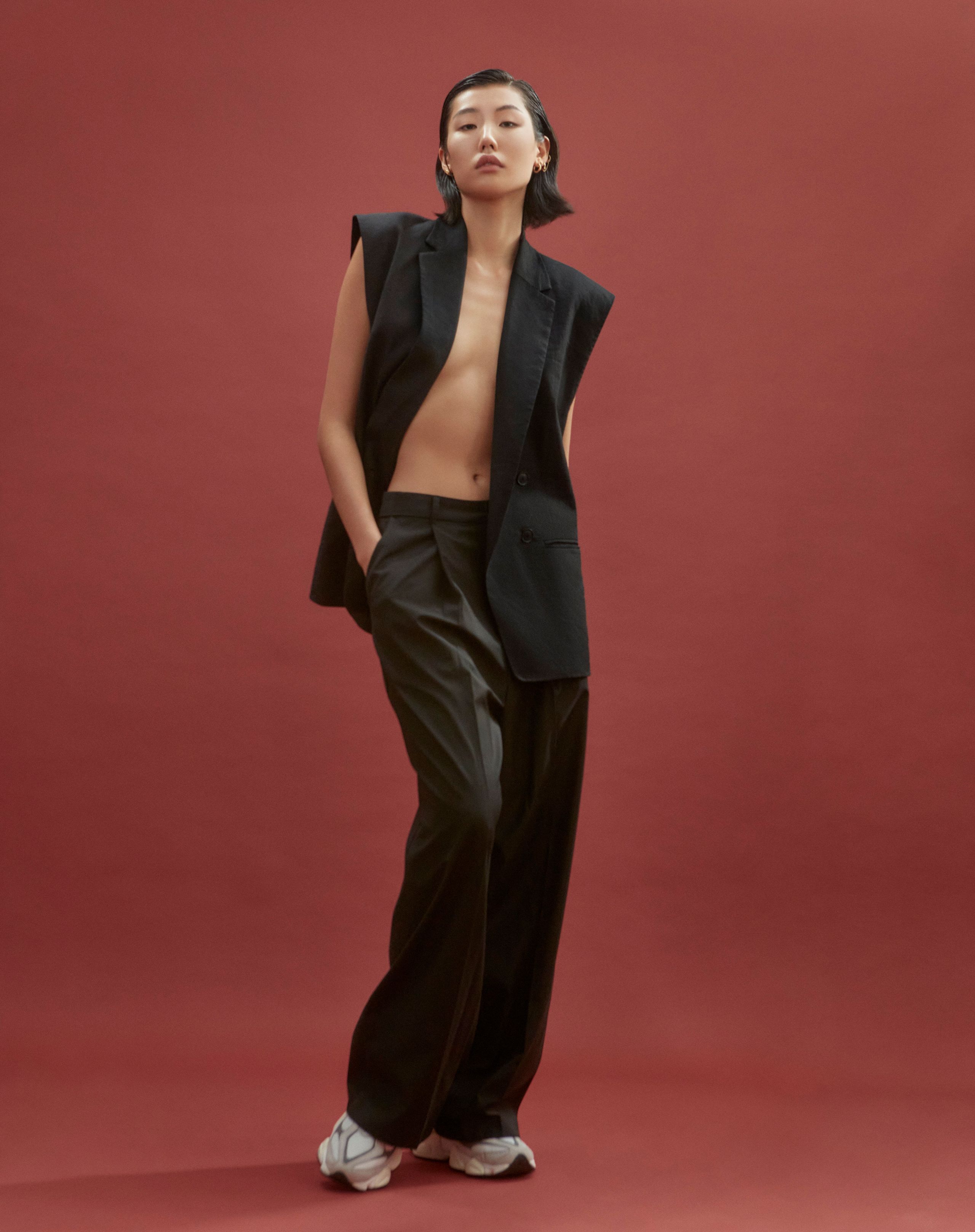 Jeannie Jay Park standing in a black suit vest worn open, pleated trousers and white sneakers