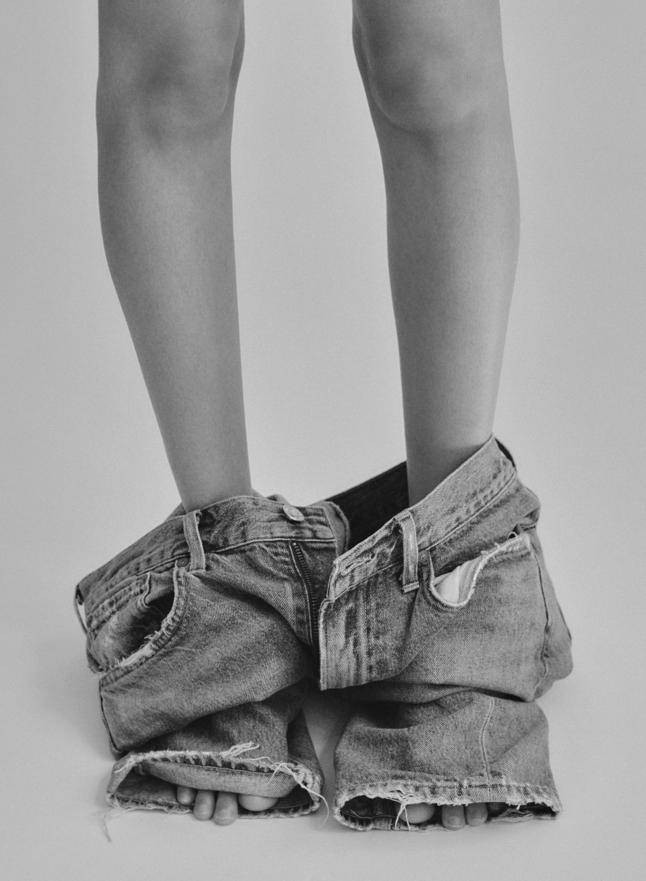 Black-and-white crop of Symon’s legs, frayed denim jeans pooled around her ankles, by New York fashion photographer Roman Yee