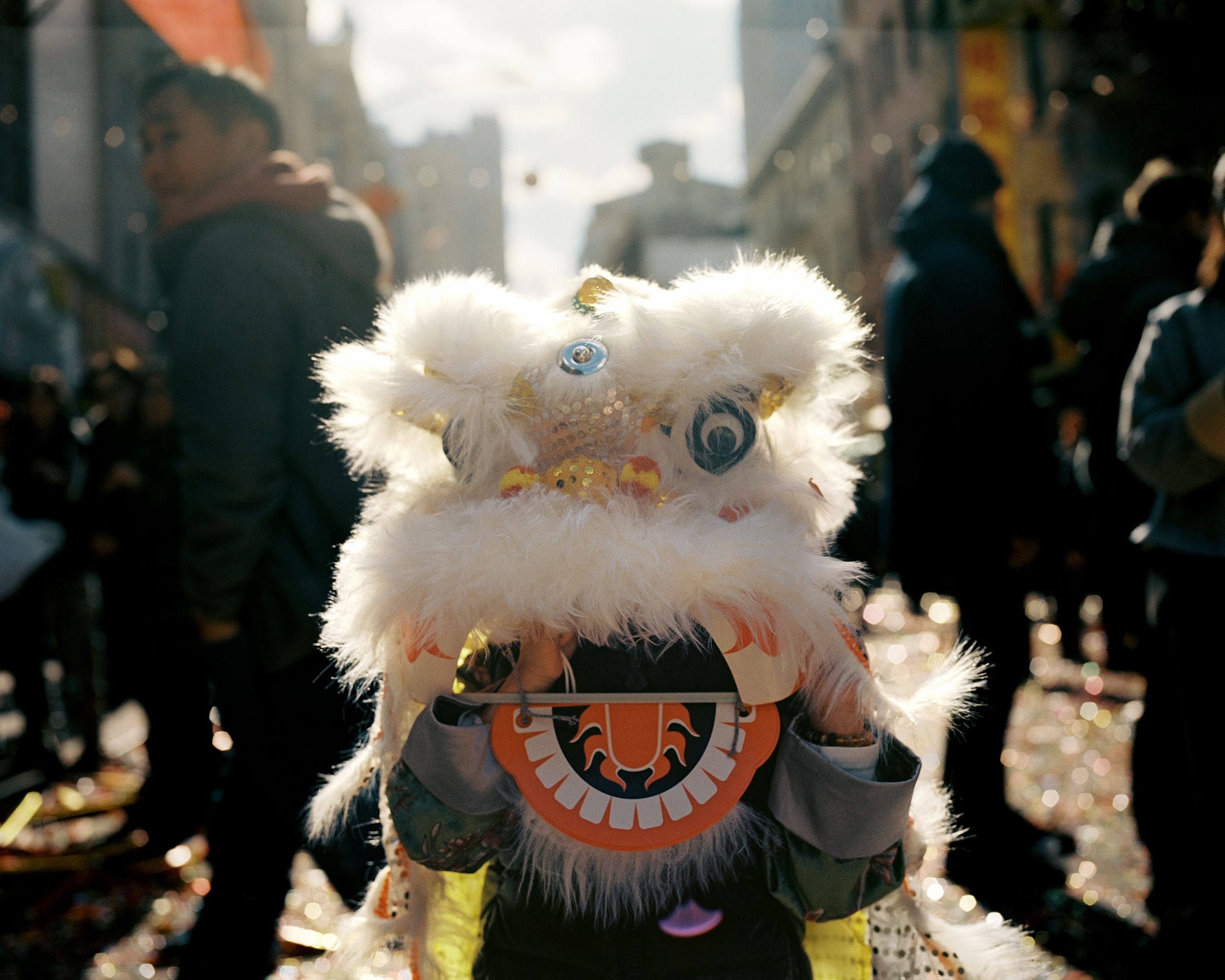Sunlit white lion dance head moving through the crowd, long shadows on the street