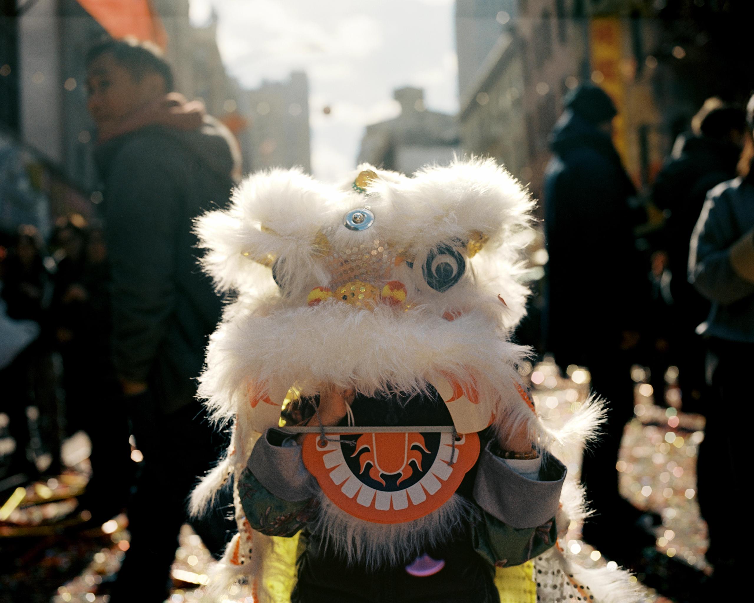 Sunlit white lion dance head moving through the crowd, long shadows on the street