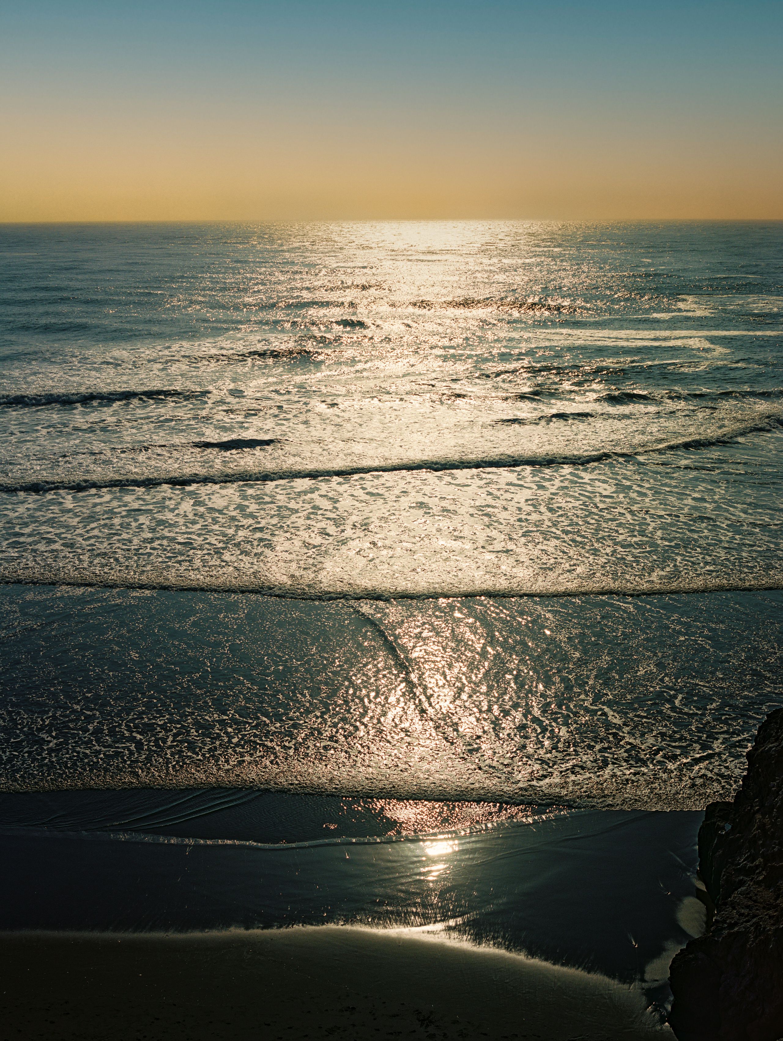 Late sun glittering on the Pacific as waves wash over dark sand
