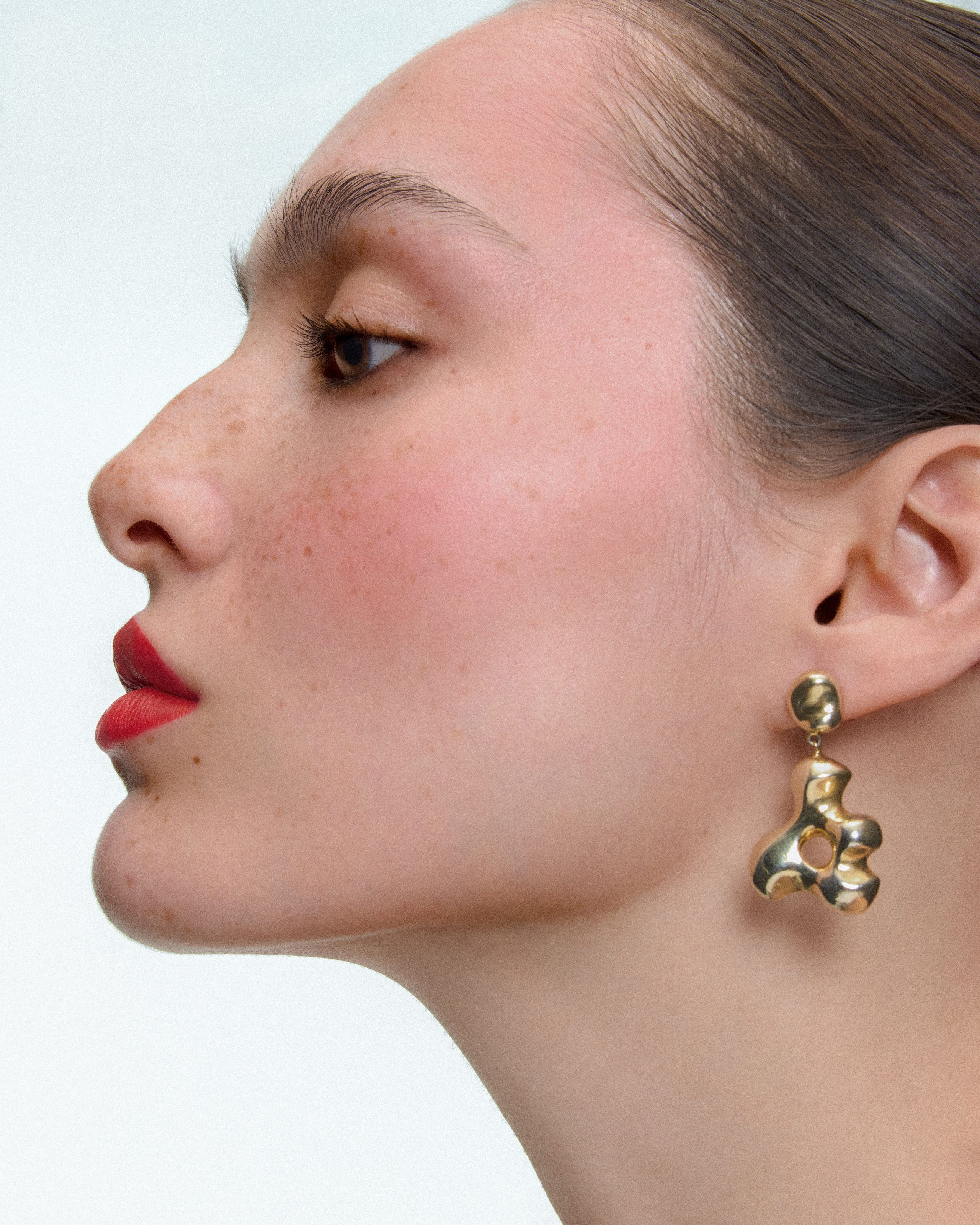 Profile of Siobhan with chin lifted, red lips and a sculptural gold AGMES drop earring