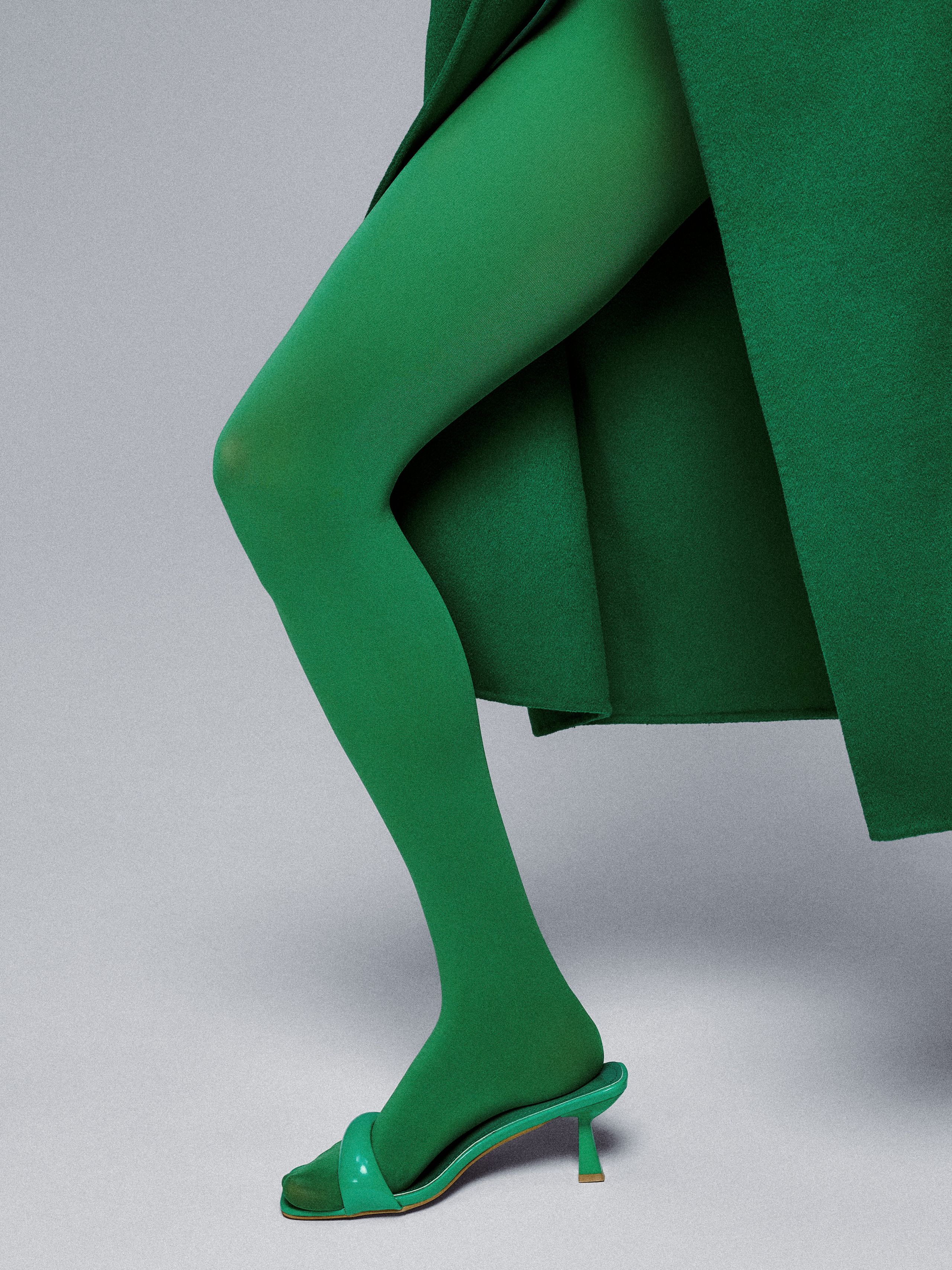 Sasha Kichigina mid-step in green tights and mint mules beneath the hem of a long green coat