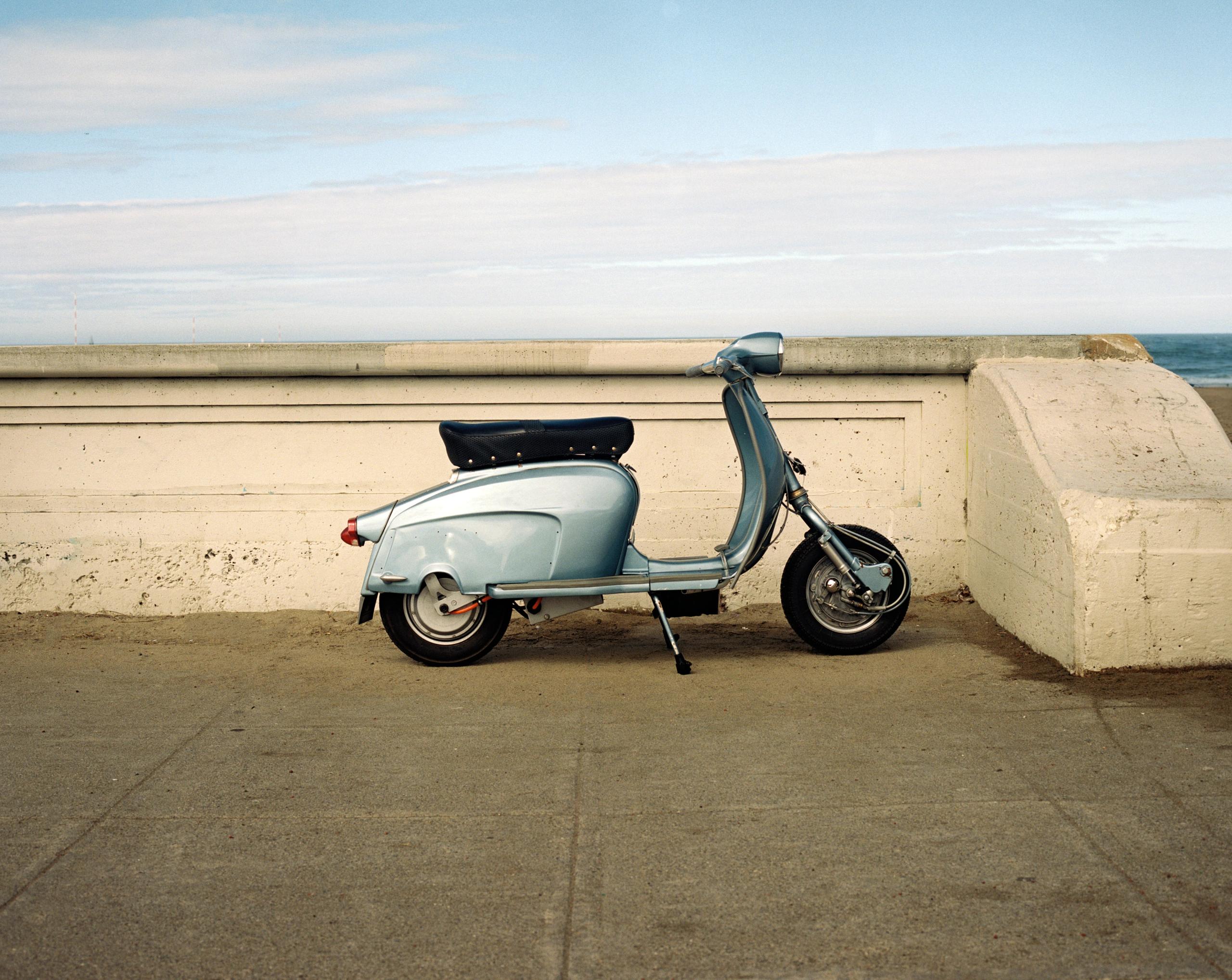 A pale blue vintage scooter parked against a concrete seawall