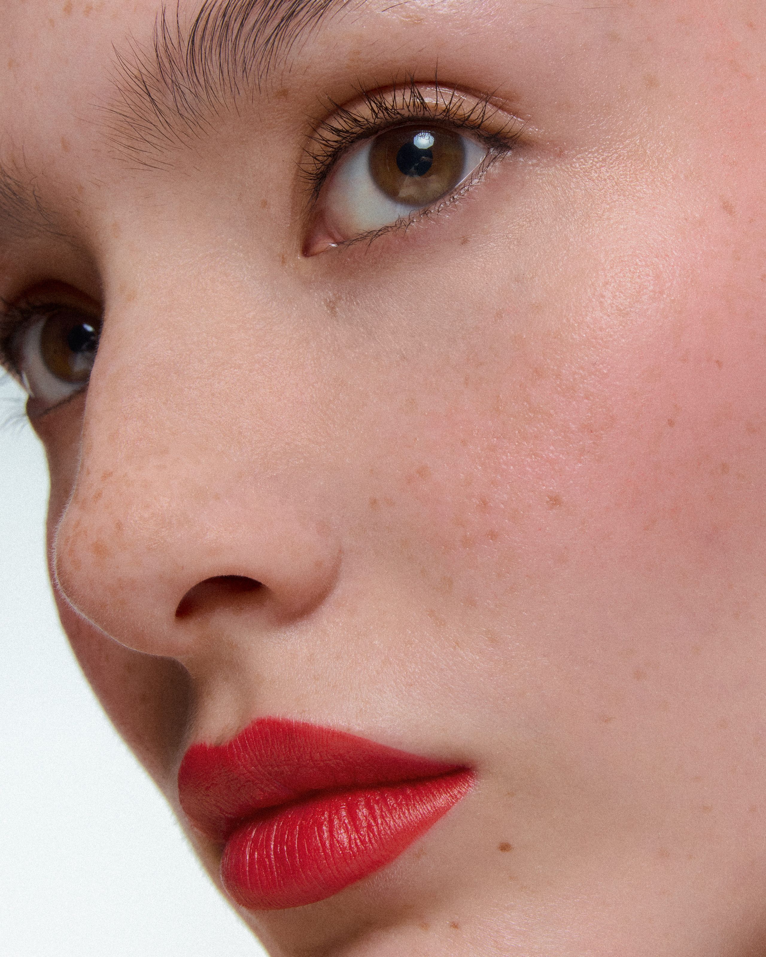 Extreme close-up of red matte lips and freckled skin, one hazel eye catching the light