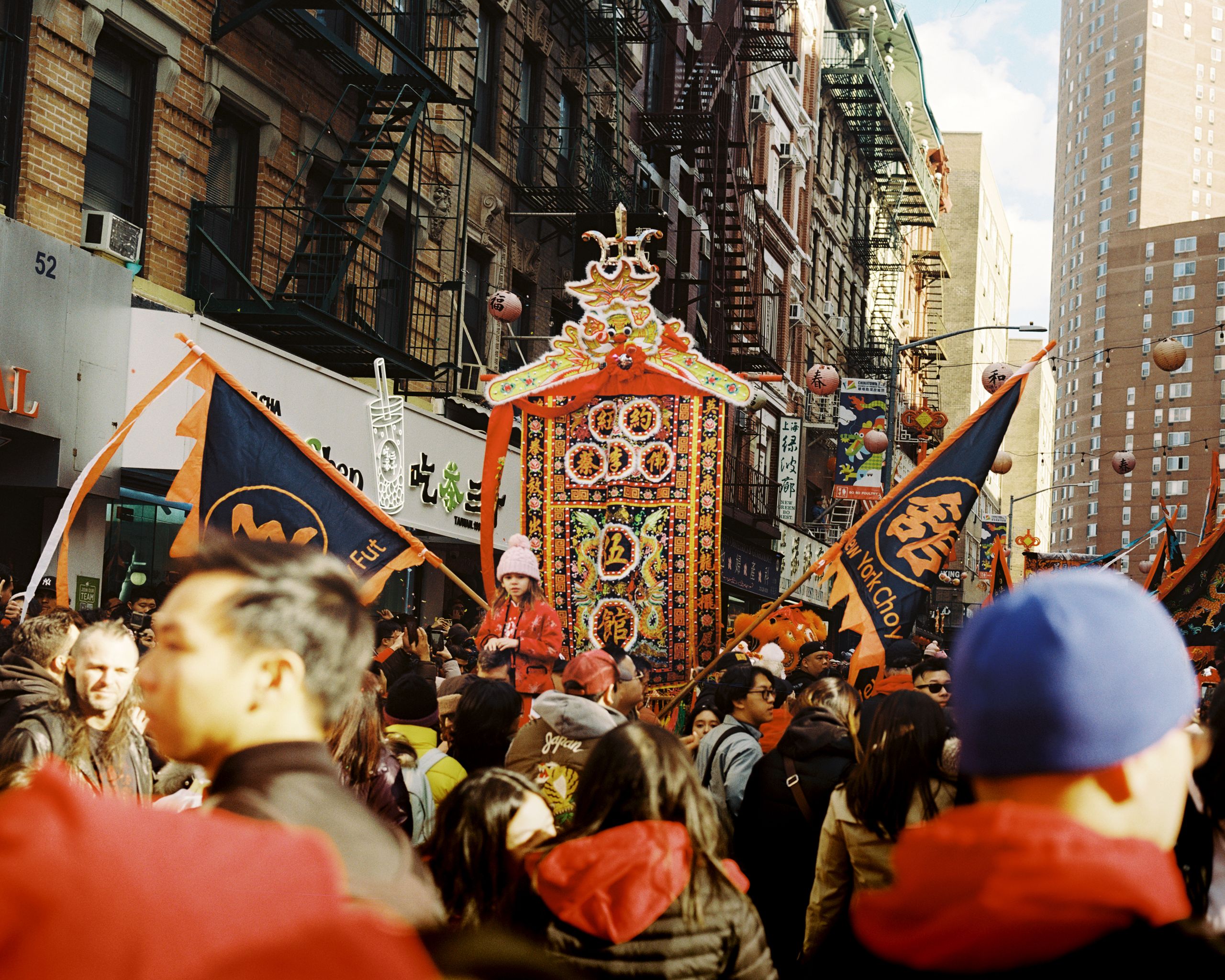 Ornate ceremonial palanquin and flags carried above the crowd between apartment buildings