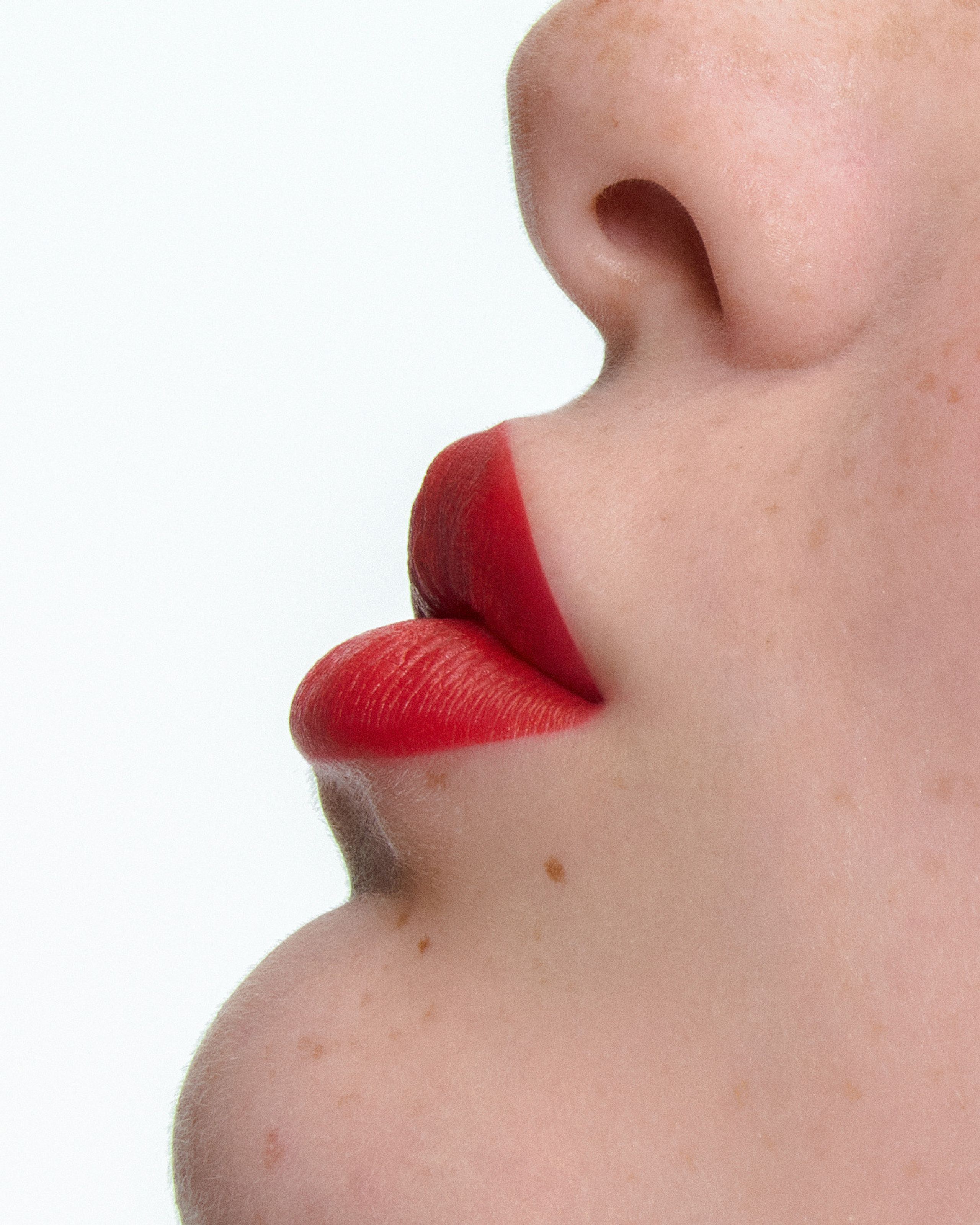 Tight profile of red lips and a freckled cheek against a white background