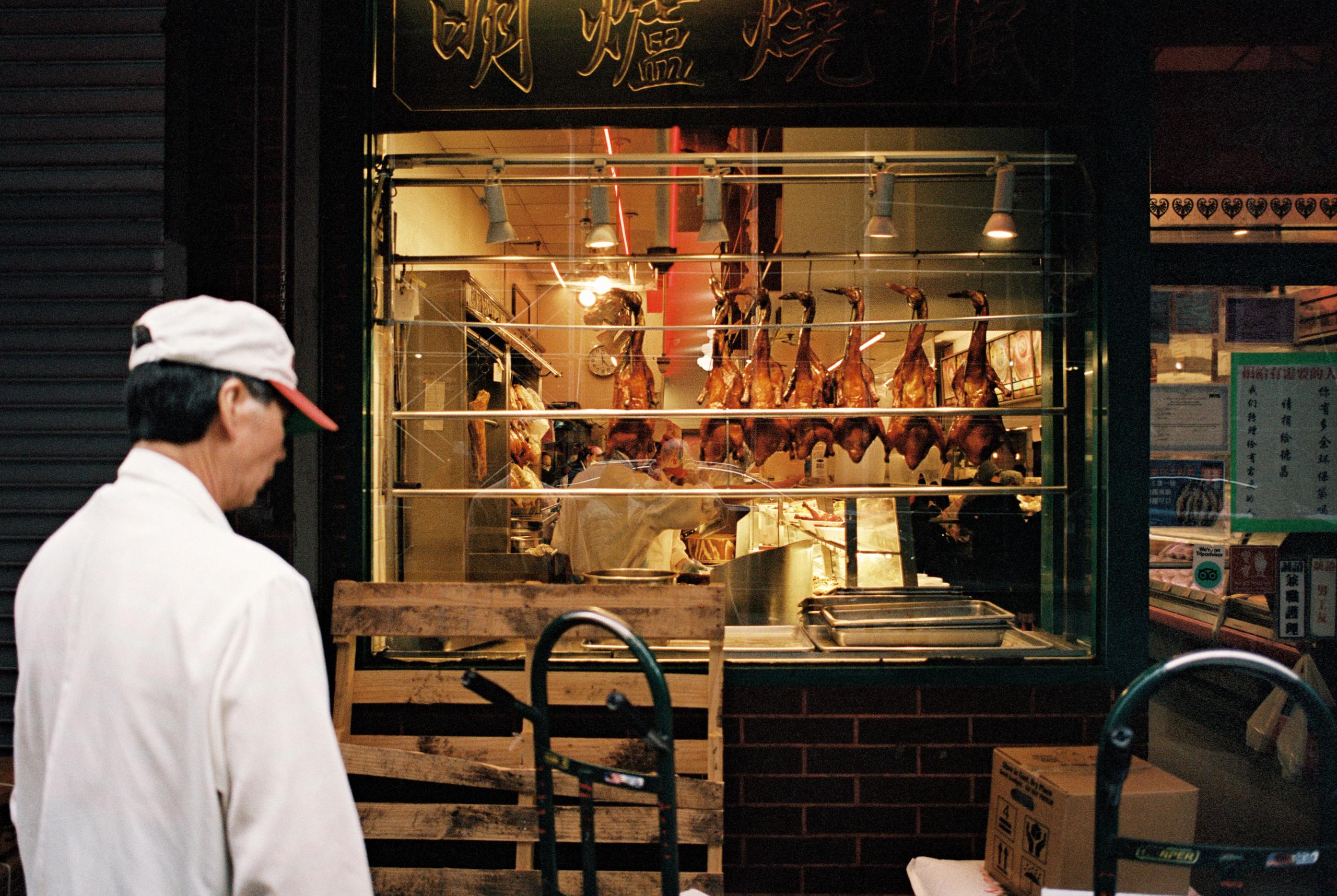 A man in a white cap passes a shop window hung with roast ducks in Chinatown