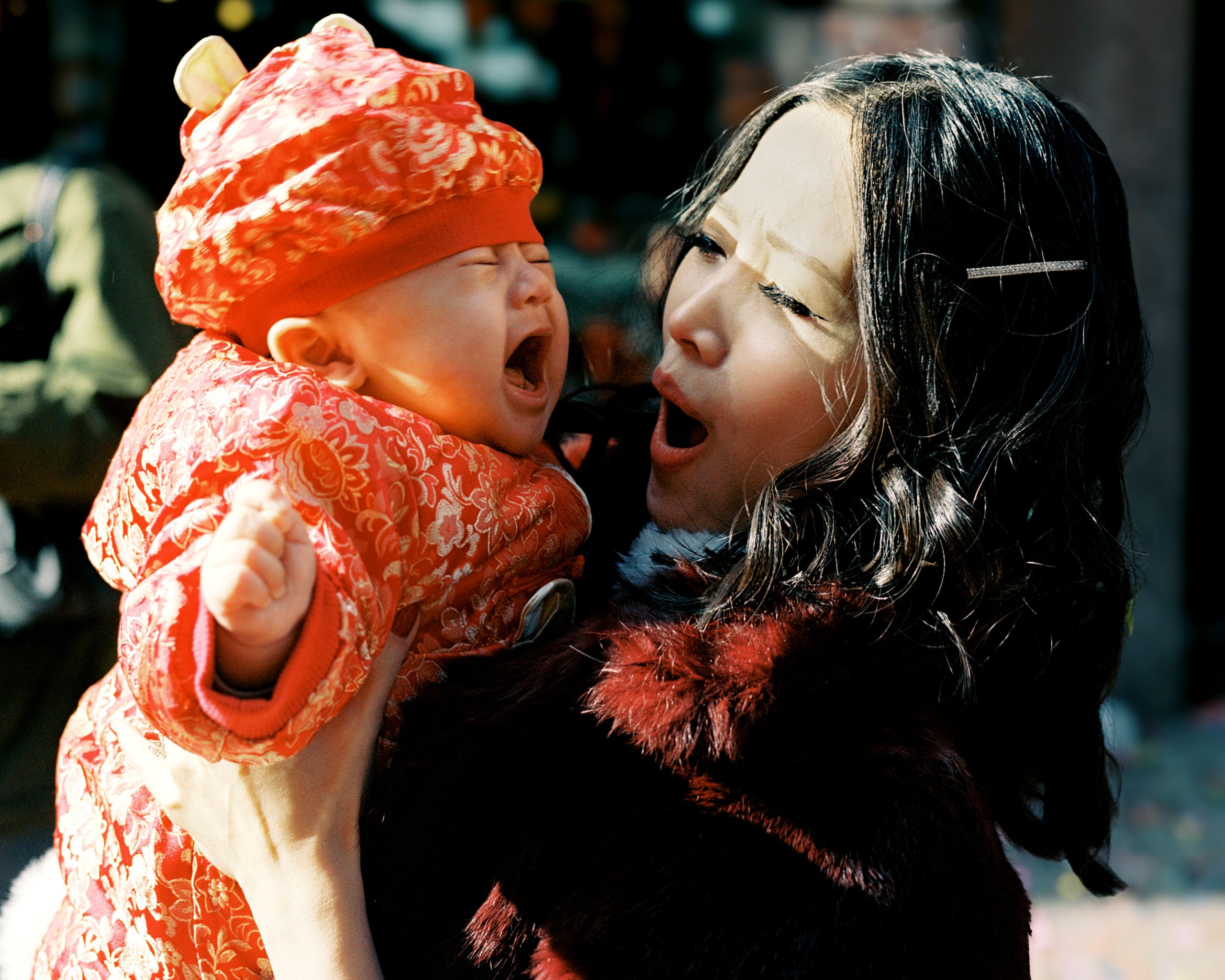 Mother lifting a laughing baby in a red knit hat and padded jacket