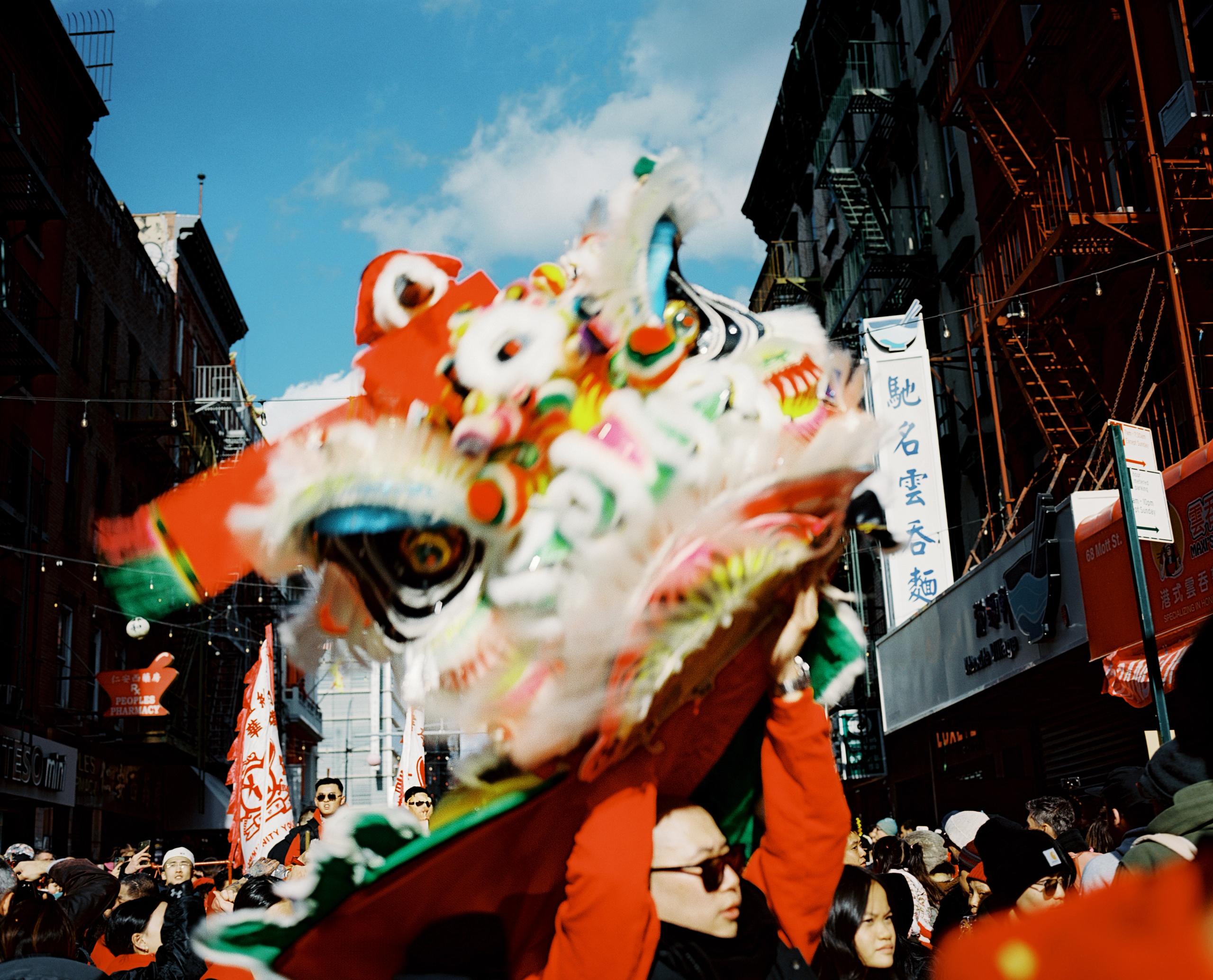 Red and white lion dance head against blue sky and fire escapes