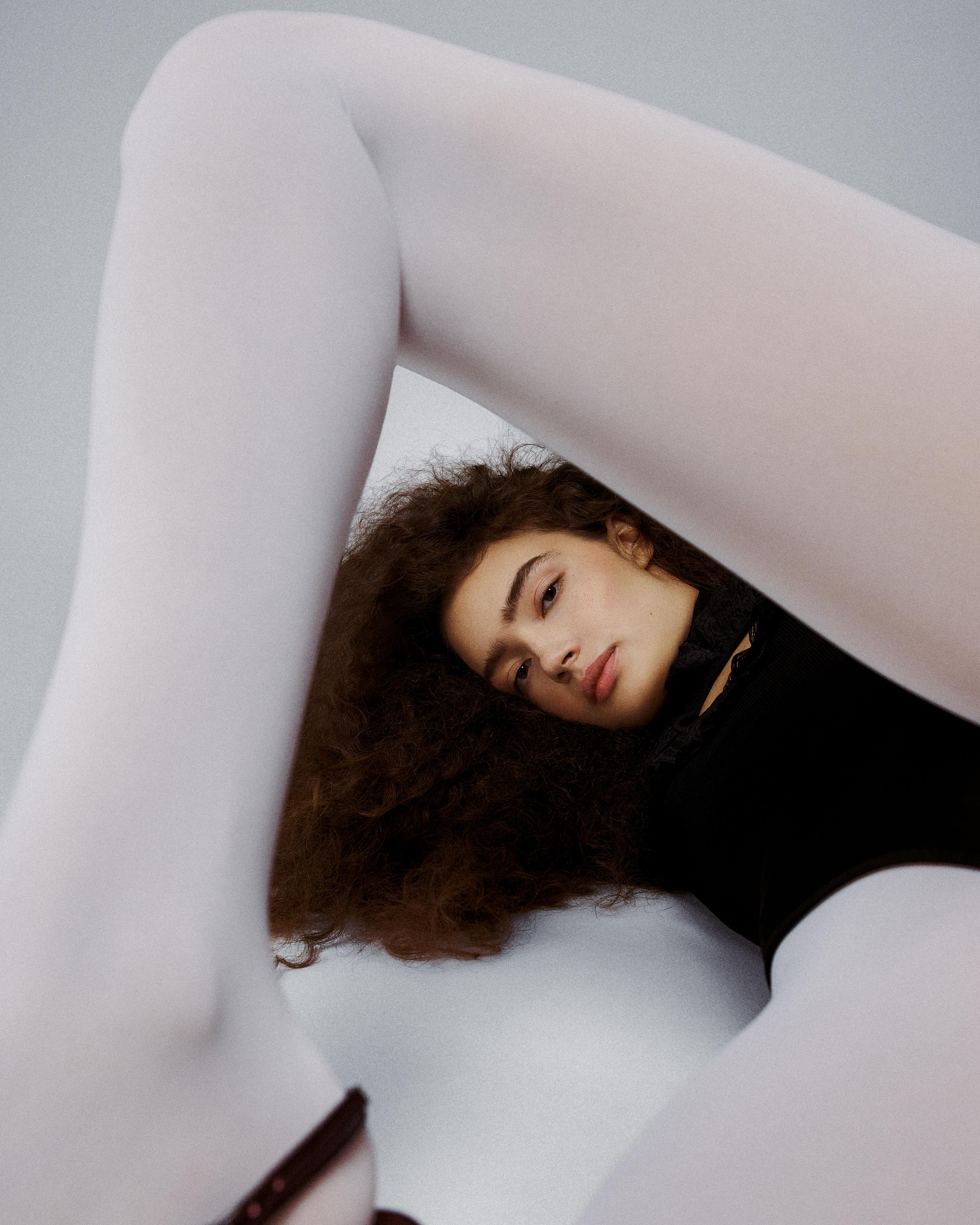 Sasha Kichigina lying on the floor in opaque white tights, legs raised, fashion editorial by New York photographer Roman Yee