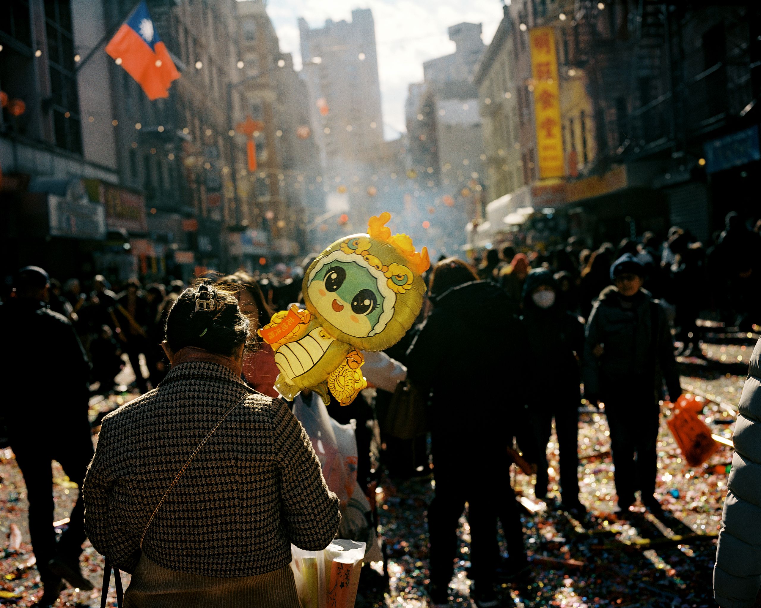 Smoke and confetti drifting above a packed Chinatown street, a golden lion head in the crowd
