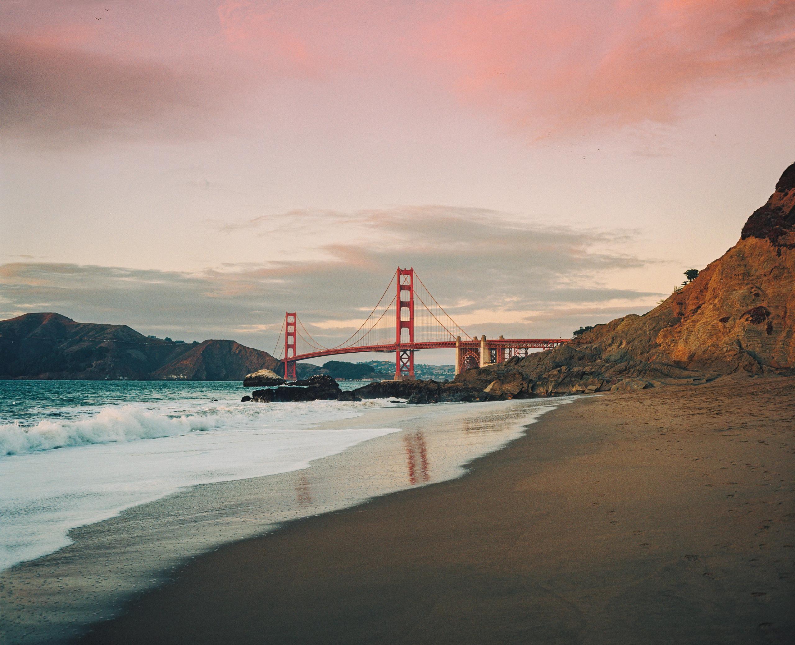 Baker Beach at dusk with the Golden Gate Bridge spanning the bay beyond the bluffs