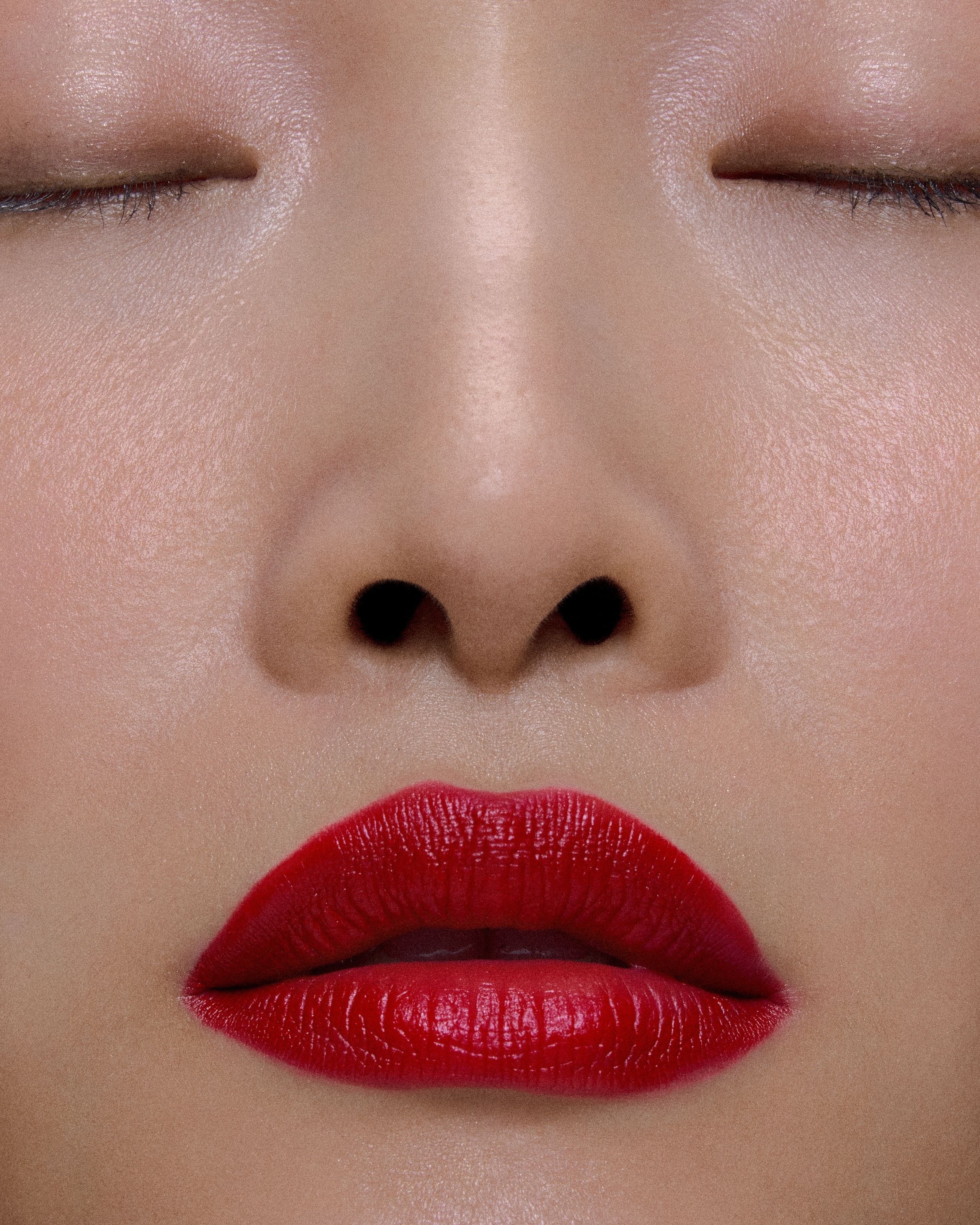 Eyes closed, glossy red lips centered in a tight crop of luminous skin