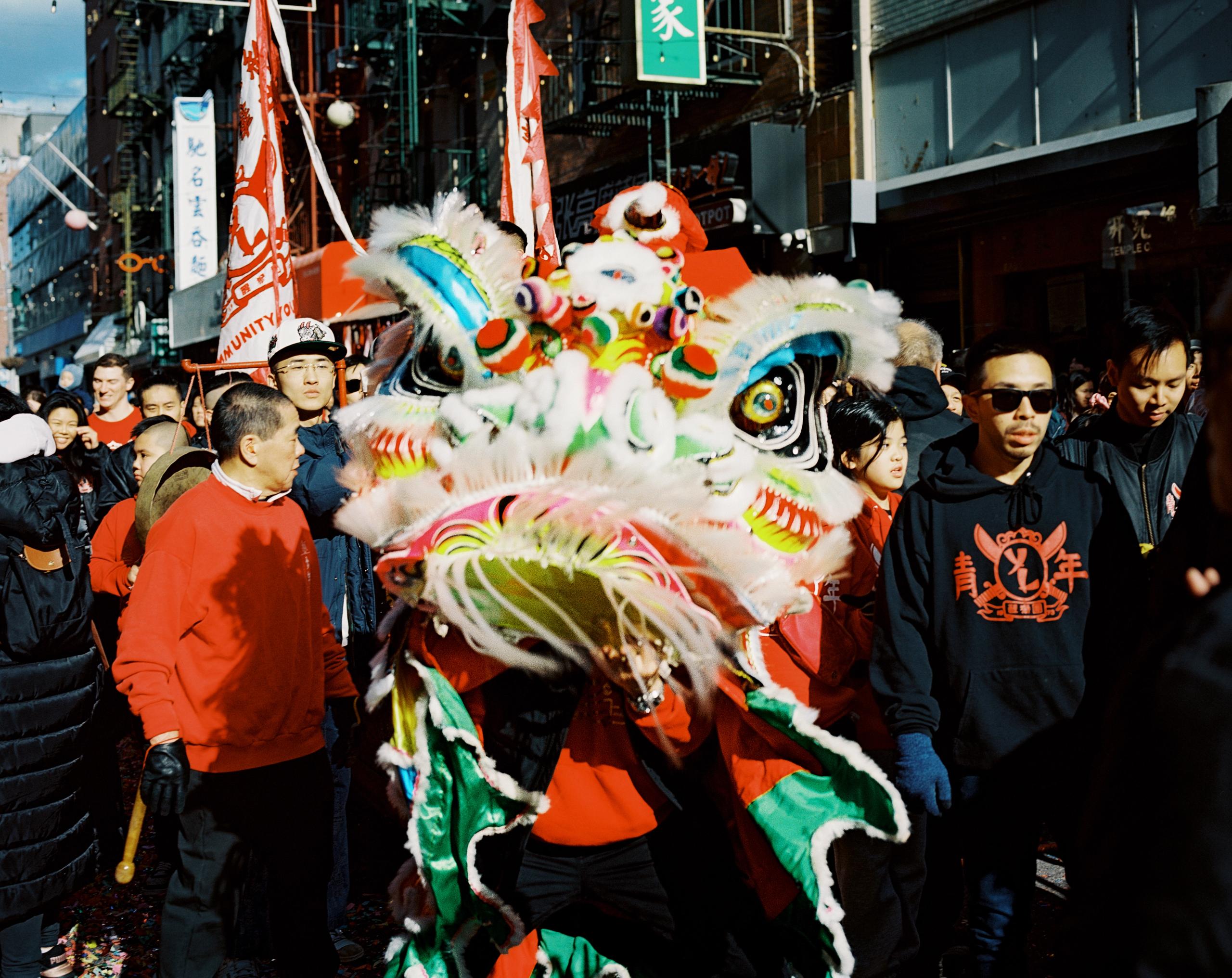 Multicolored lion dance head surrounded by spectators in red and black