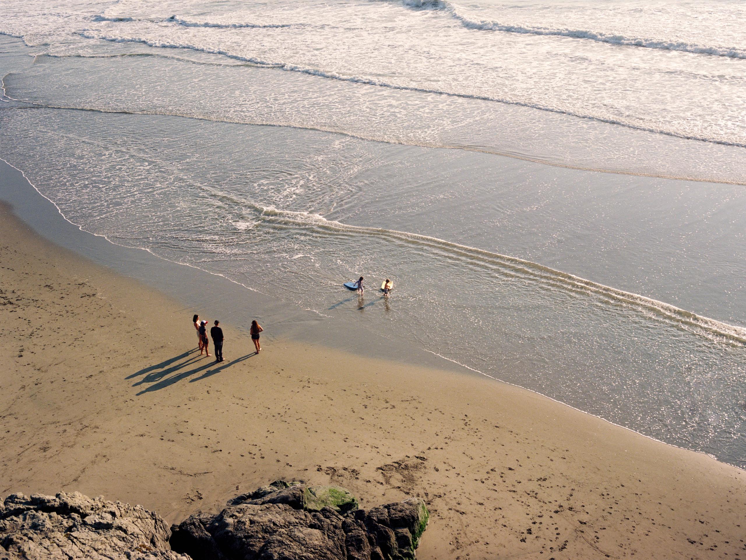Three people walking the shoreline at low tide, seen from the bluff above