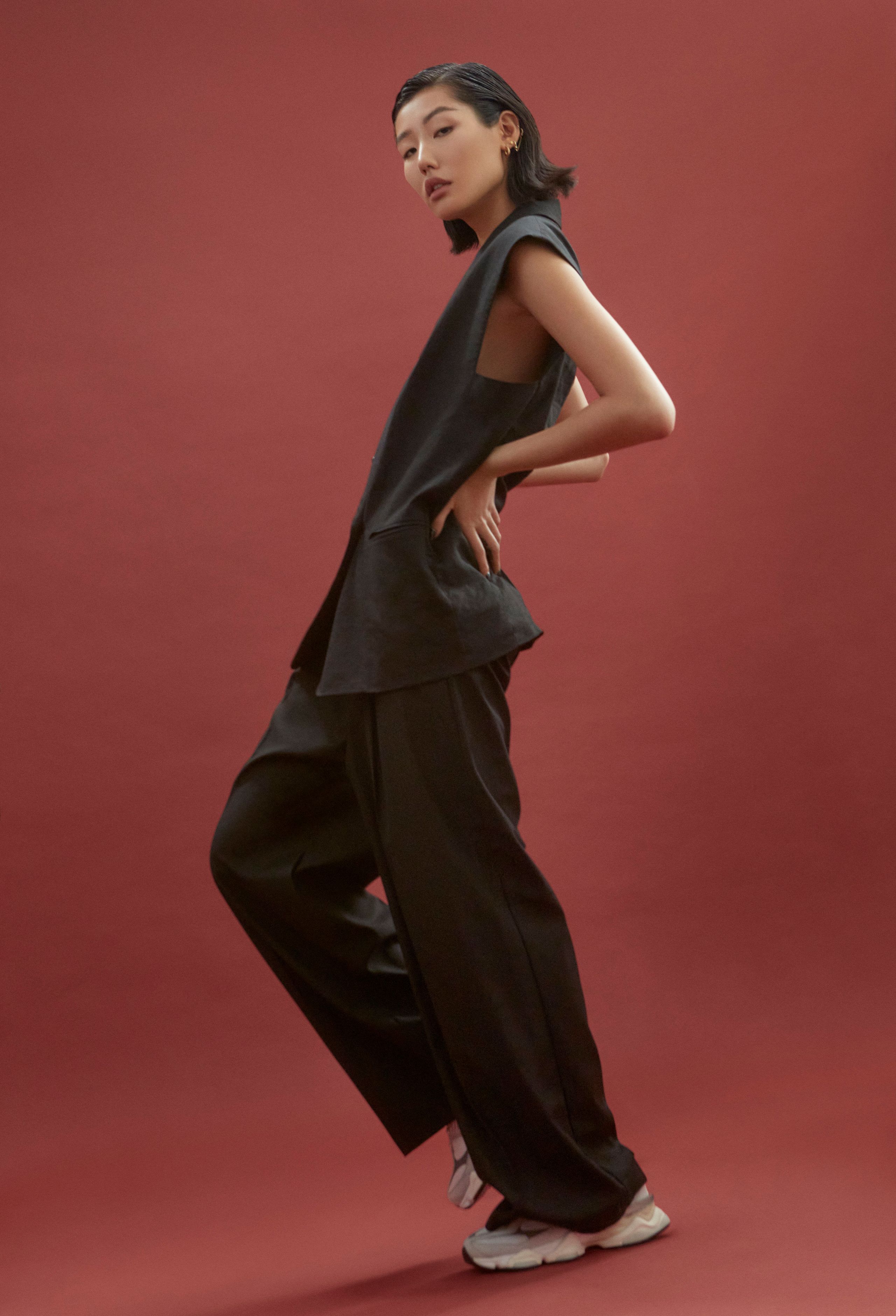 Jeannie Jay Park in a sleeveless black vest, wide-leg trousers and sneakers, hand on hip, leaning back