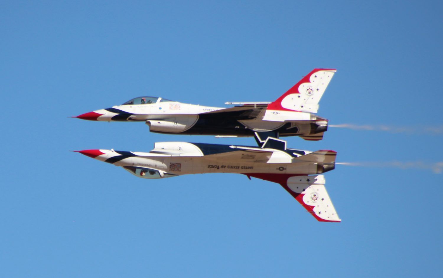 Two airplanes flying in sync with one upside down, mirroring eachother.