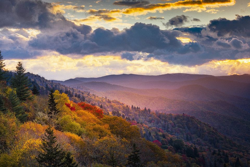 Sun beginning to set on a skyline of mountains and trees.