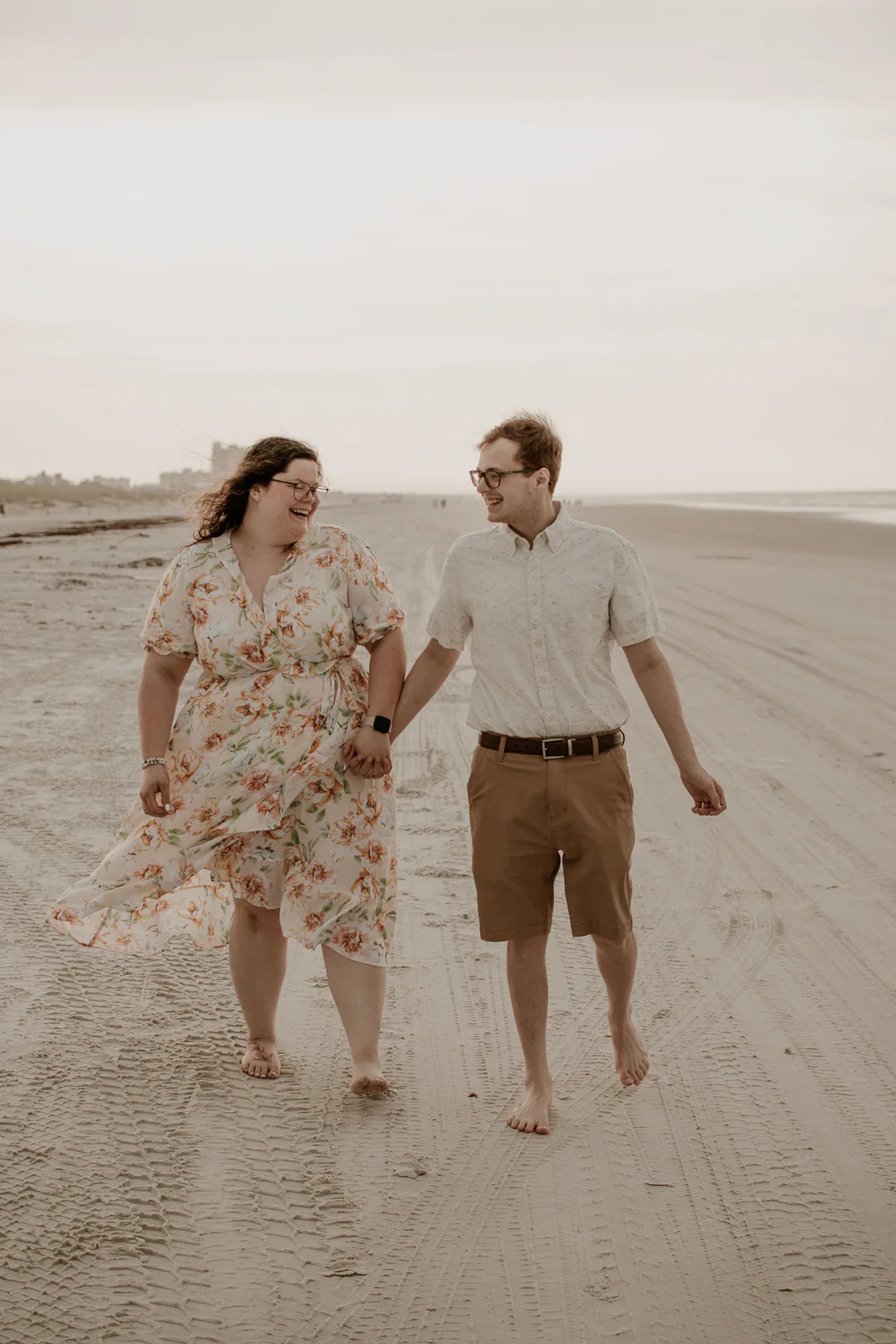 Couple walking hand in hand along a sandy beach.