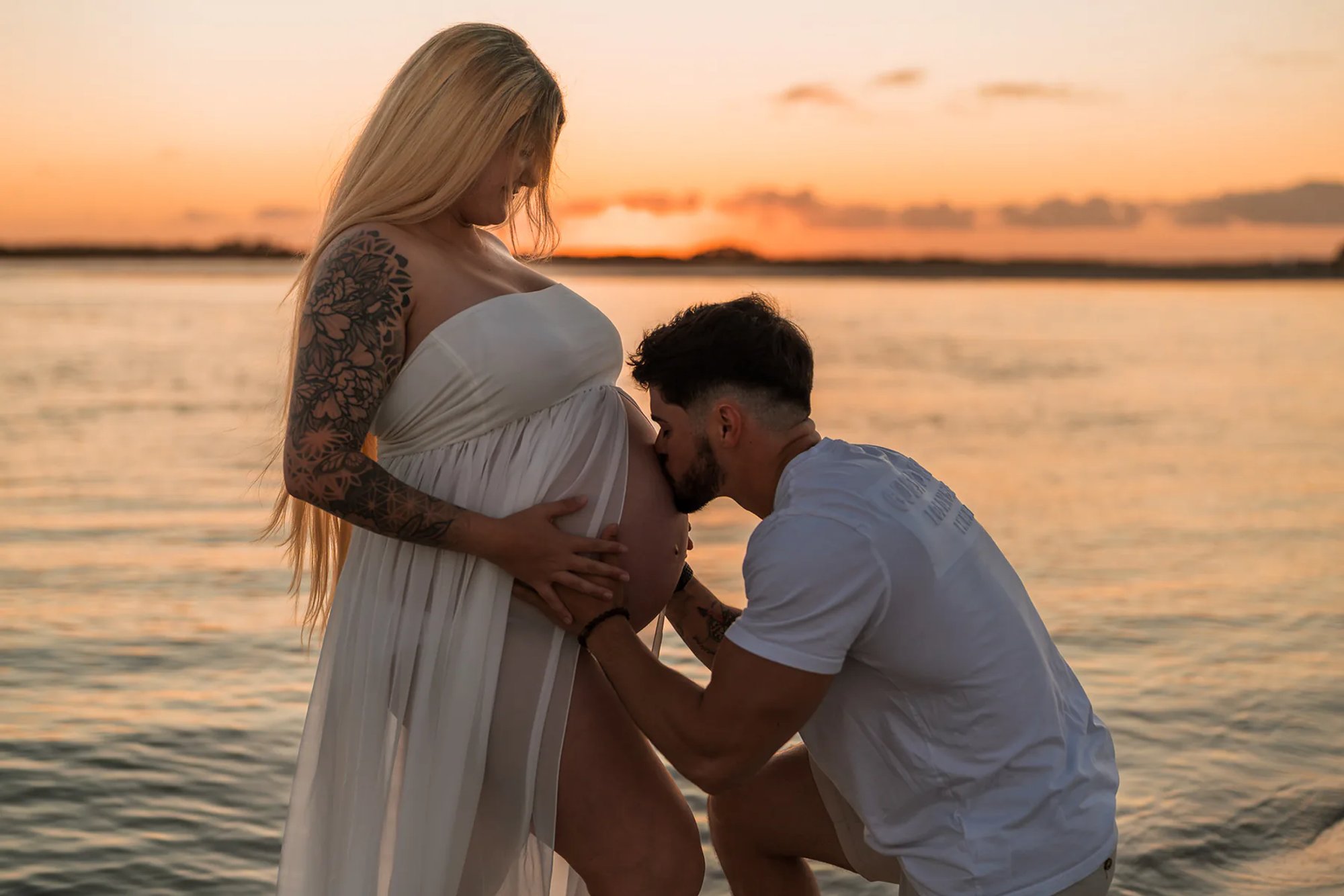 Close-up maternity photo of father kissing baby bump near the water