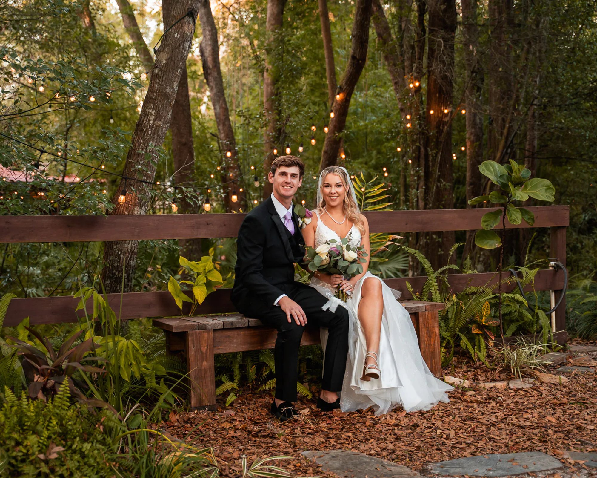 Bride and groom seated on bench under string lights at Bridle Oaks Barn in DeLand Florida