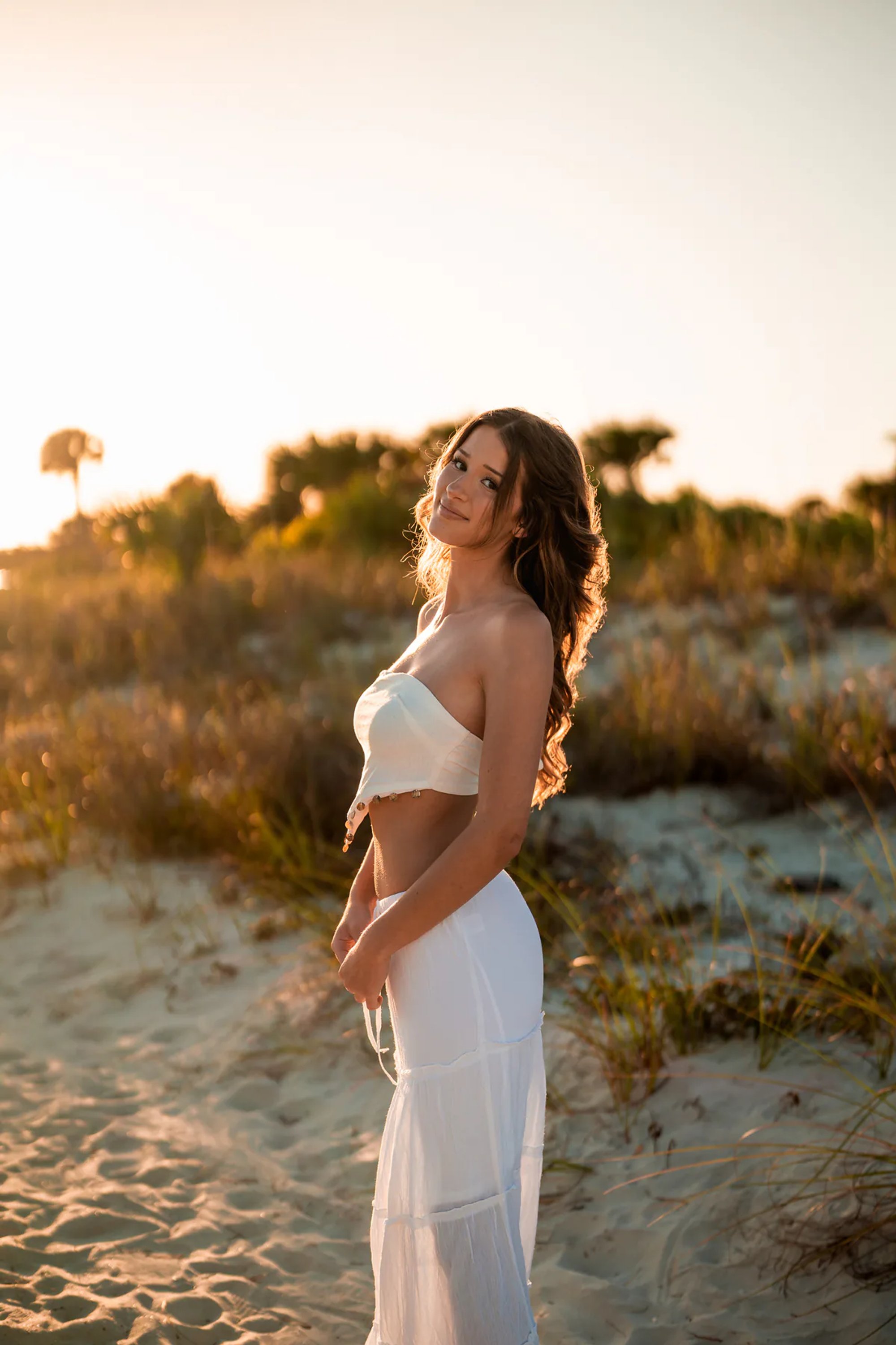 Young woman in a white outfit standing among sandy coastal dunes.