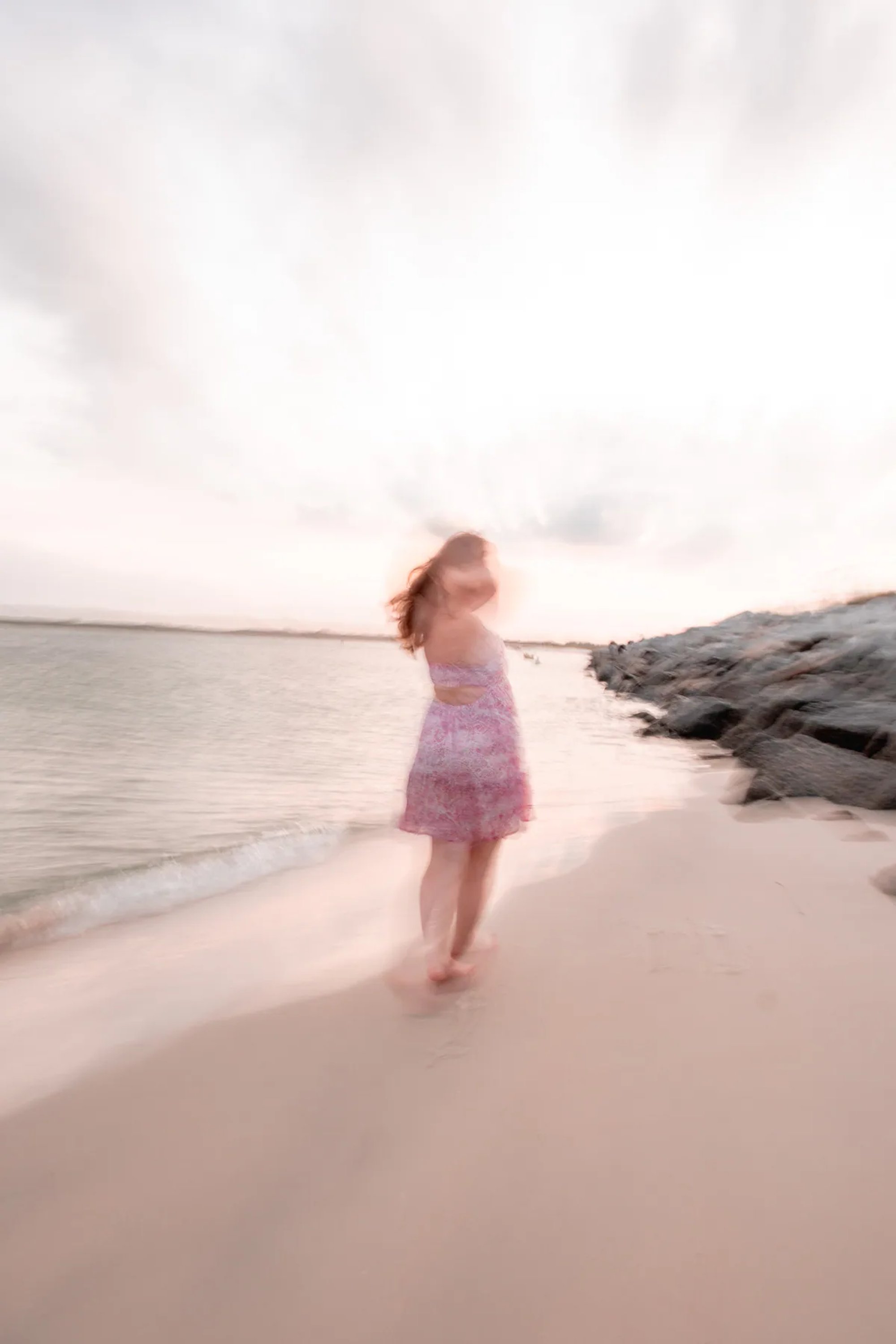 Soft-motion portrait of a woman in a pink dress walking along the beach.