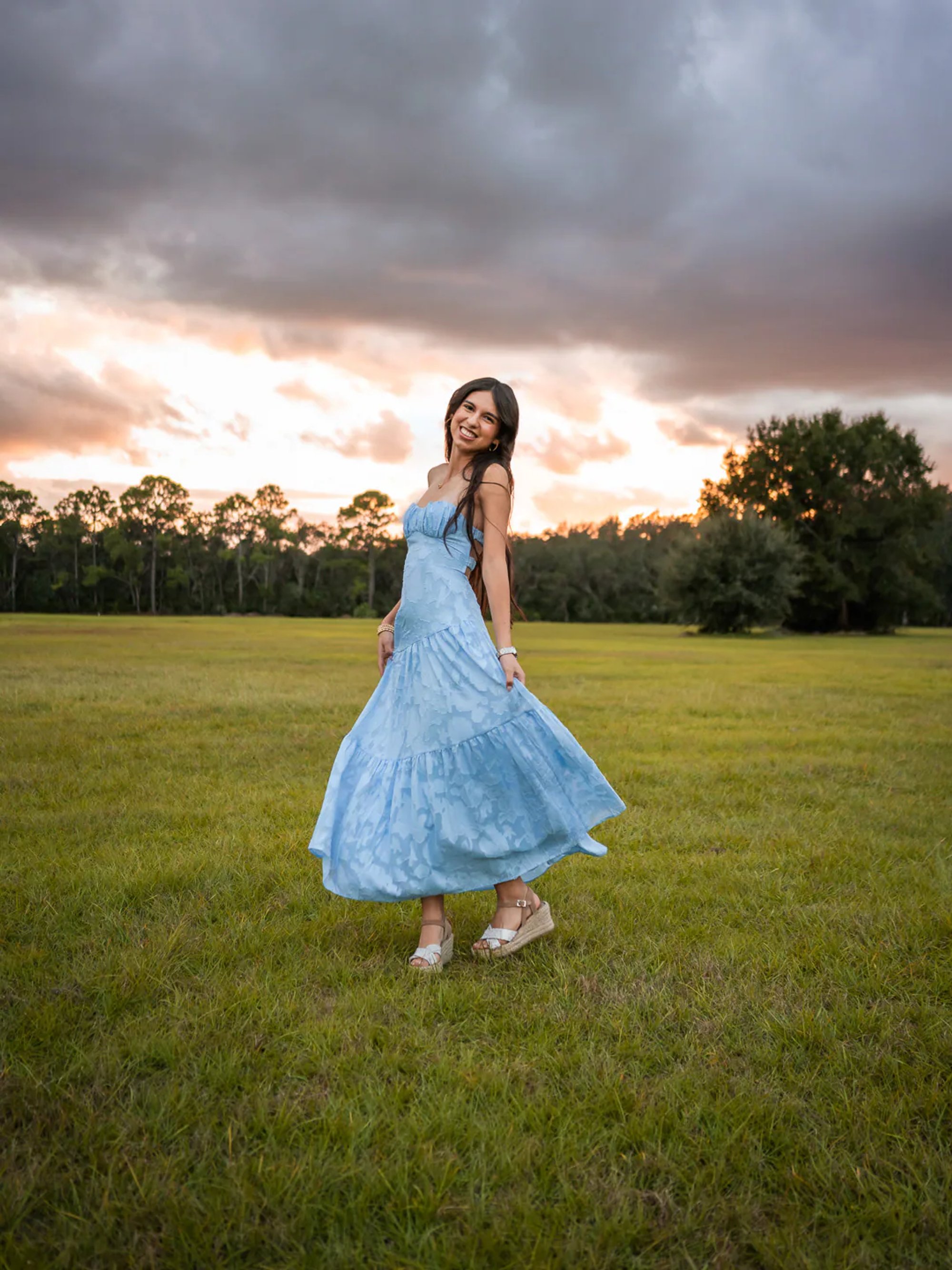 Young woman spinning in a flowing blue dress at sunset.
