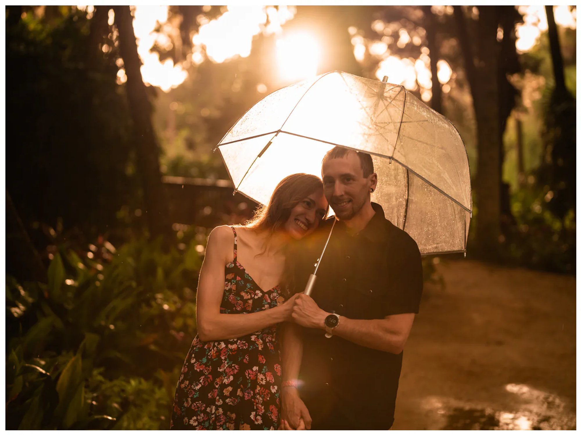 Couple sharing a close moment beneath an umbrella with golden sunlight in the background at Washington Oaks Gardens.