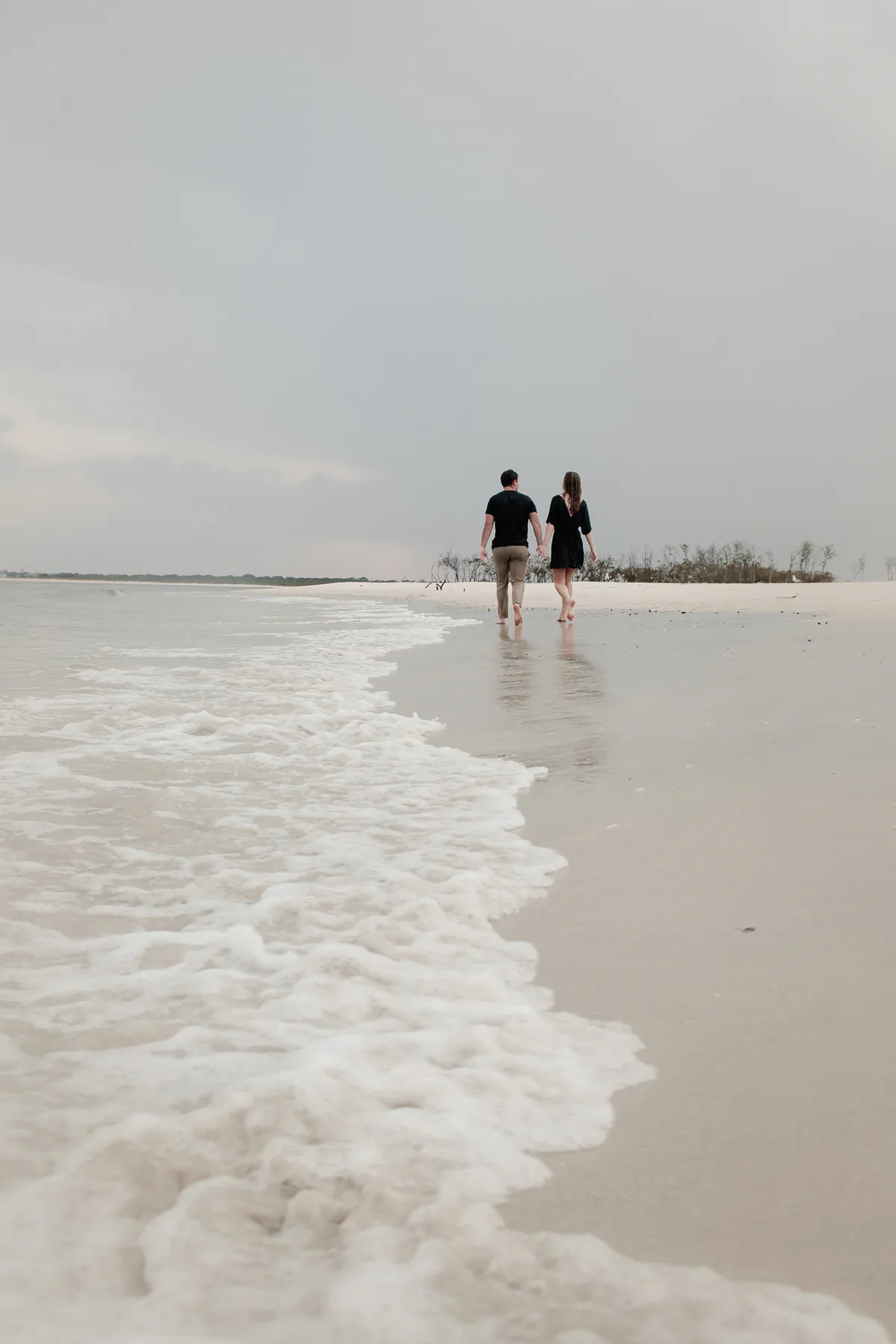 Couple walking along the shoreline during rainy engagement photos in Ponce Inlet Florida