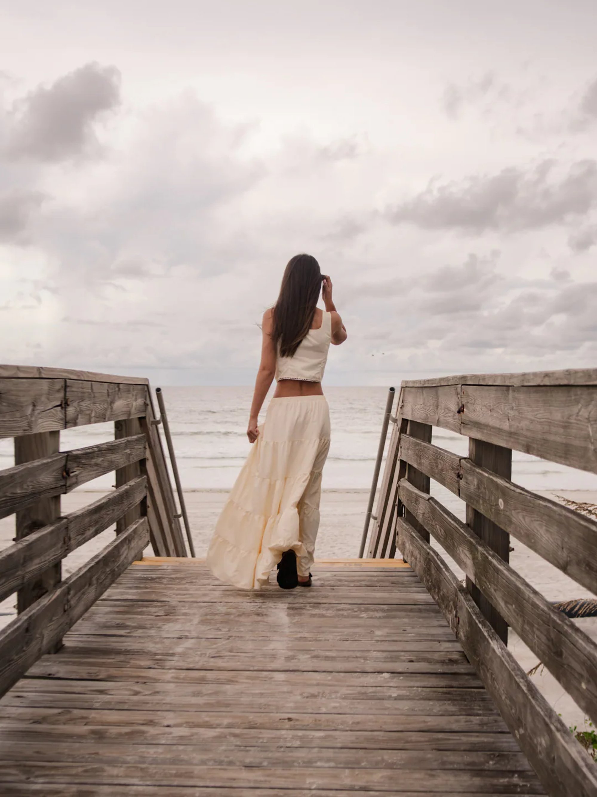 Young woman walking down a wooden boardwalk toward the ocean.