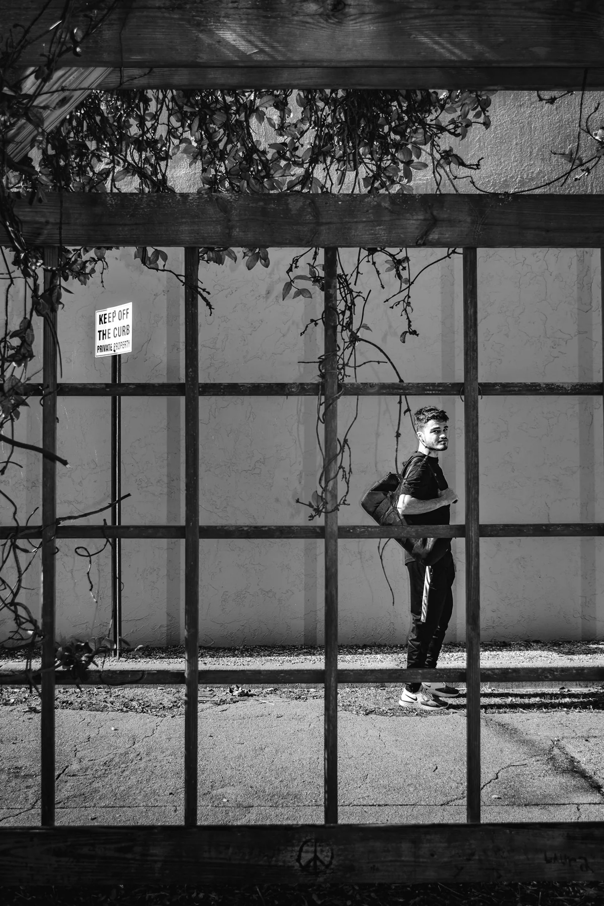 Black-and-white portrait of a person standing behind a metal gate.