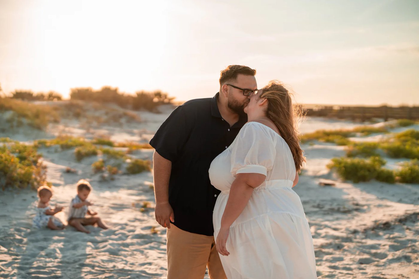 Ponce Inlet family photography session with parents kissing on the beach at sunset while children play in the sand
