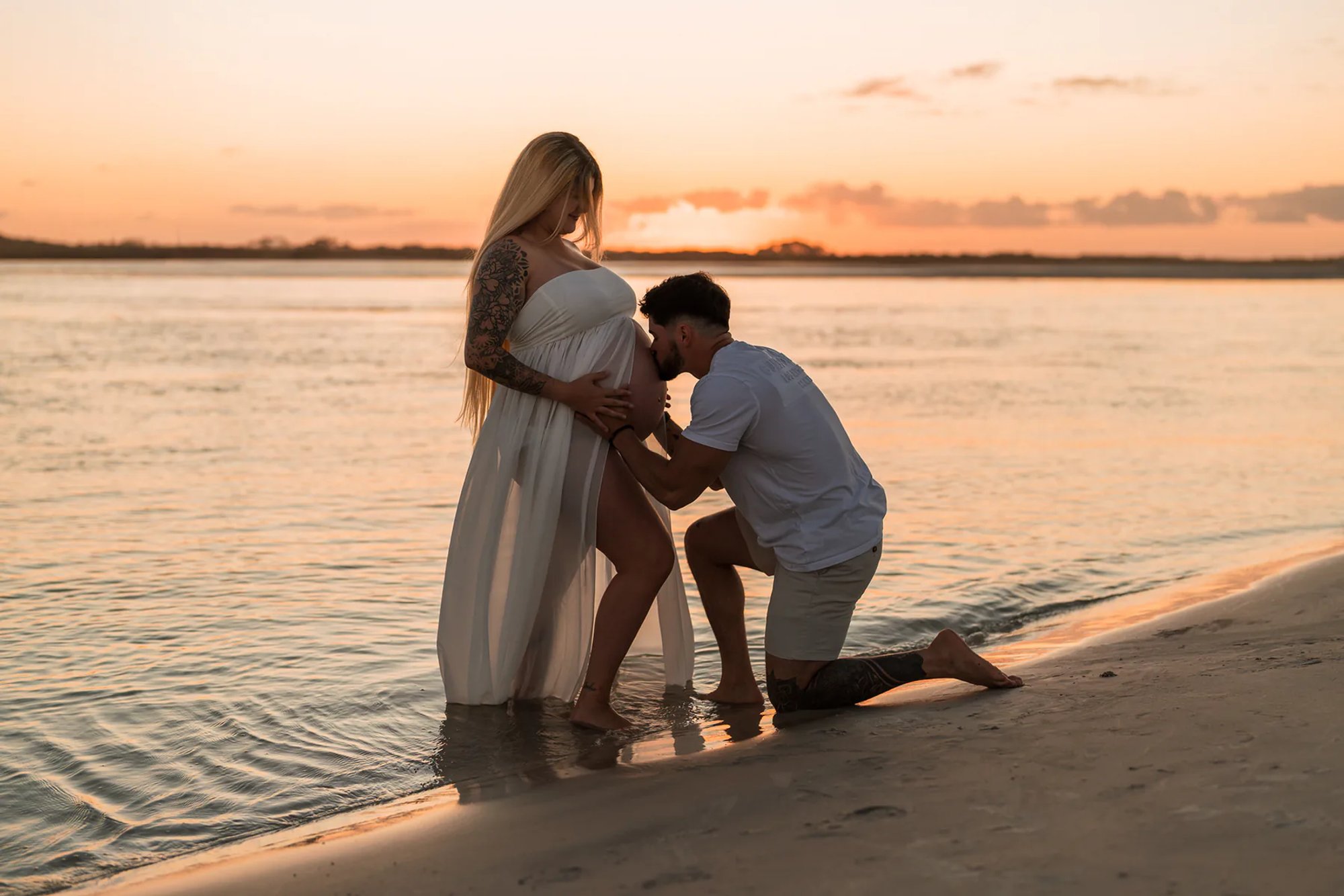 Father kneeling by baby bump during beach maternity photos in Florida