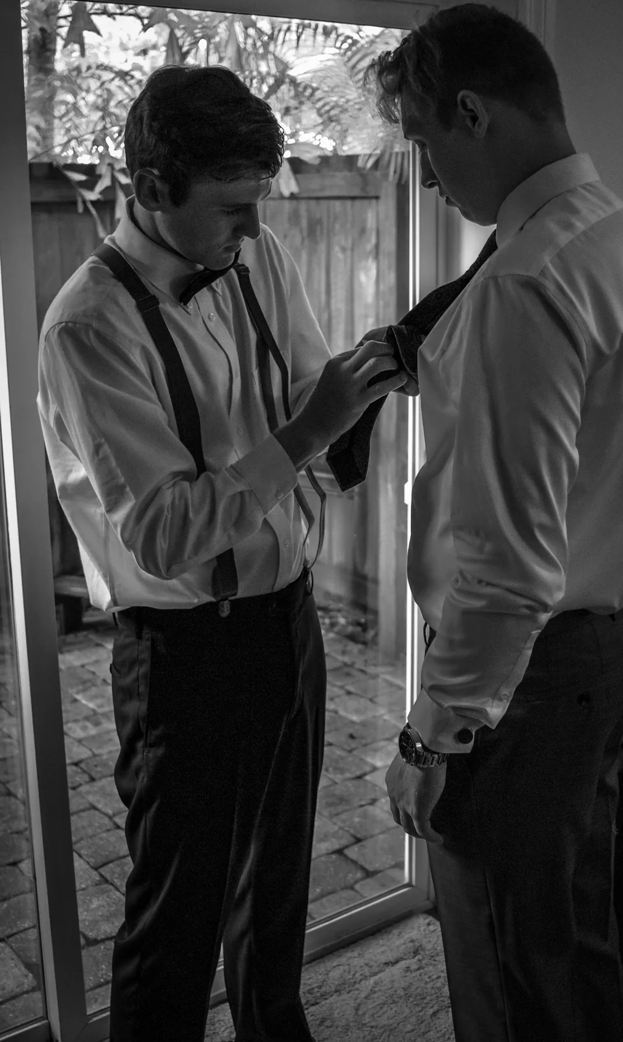 Groomsman adjusting the groom's tie in a black-and-white preparation photo.