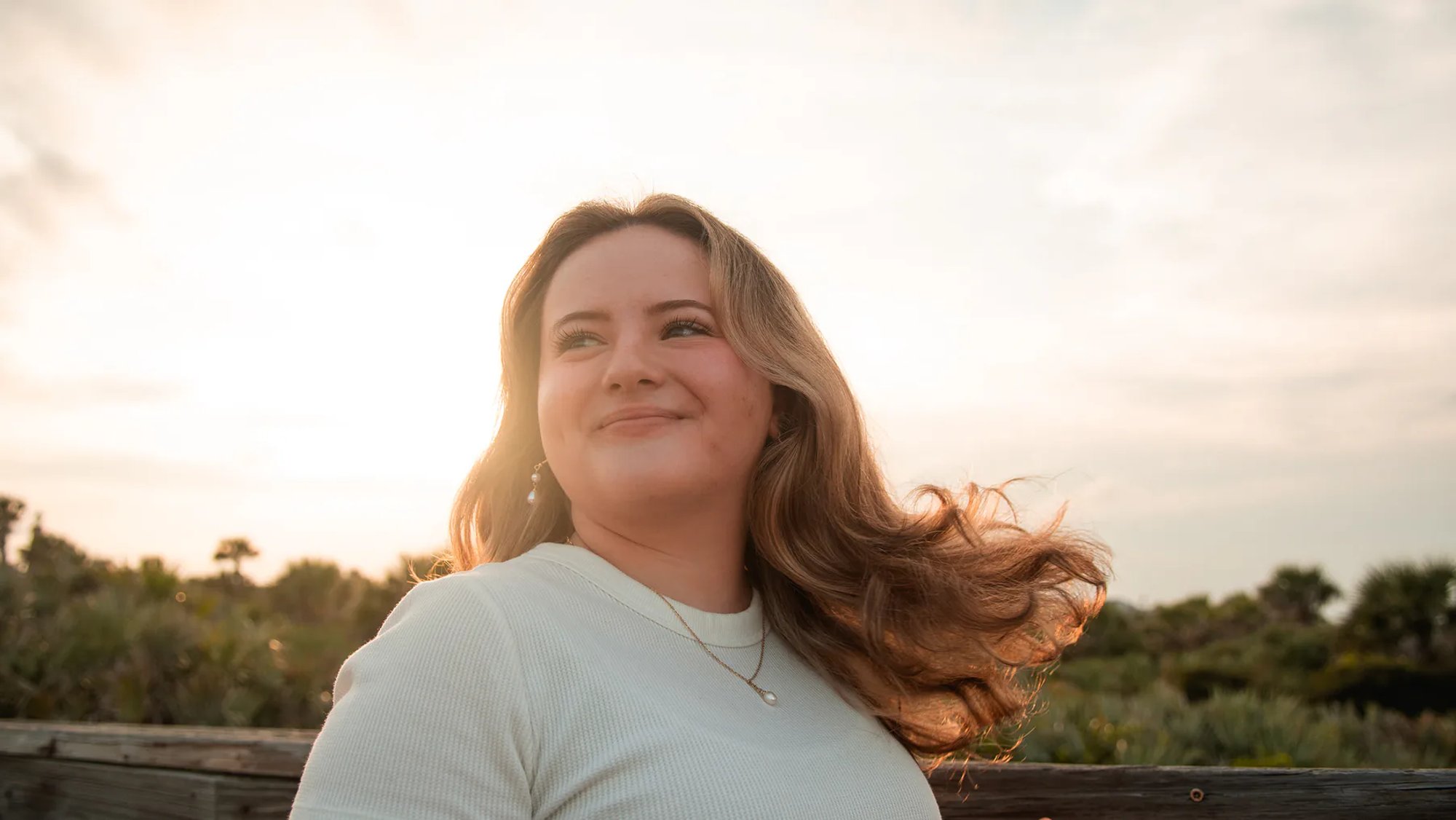 Young woman in warm sunset light near a beach boardwalk.