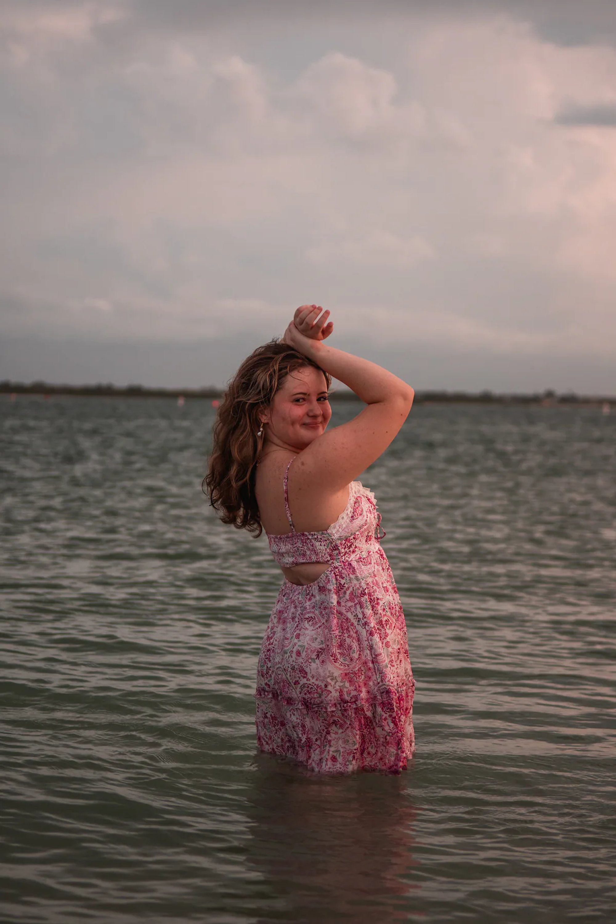 Woman in a pink floral dress standing waist-deep in calm water.