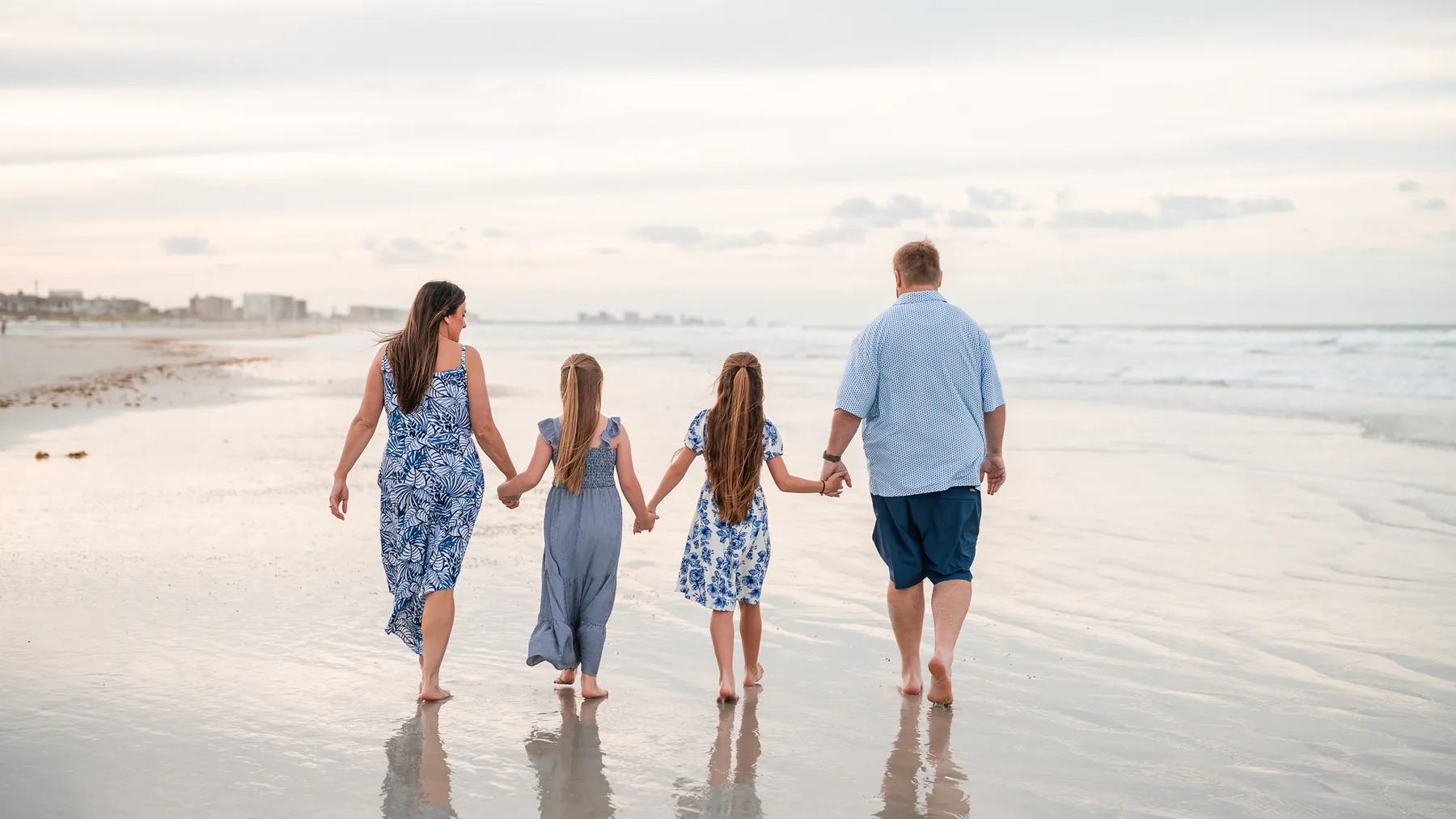 Family of four walking hand in hand along the shoreline.
