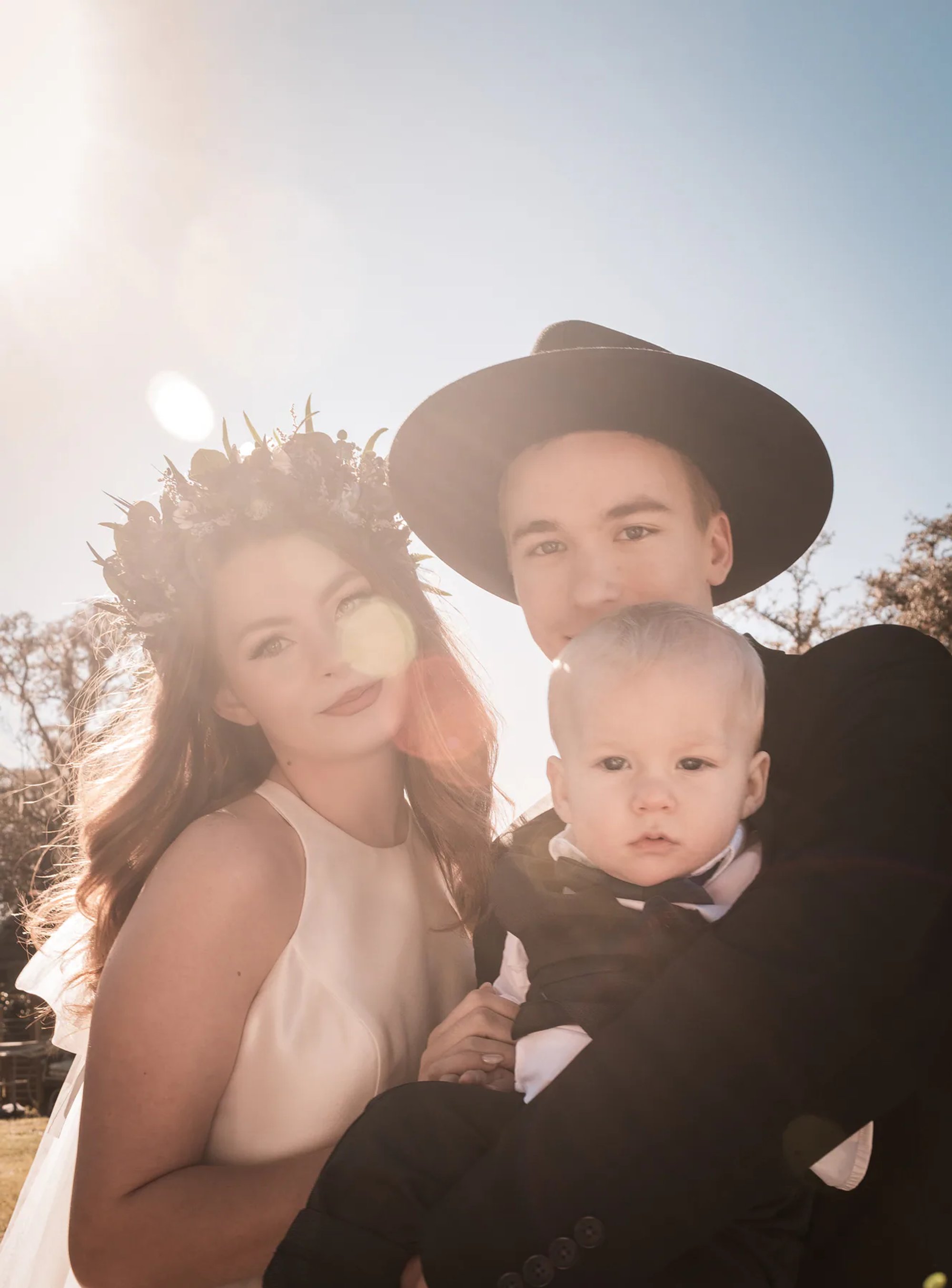 Bride and groom holding a young child during a backlit family wedding portrait.