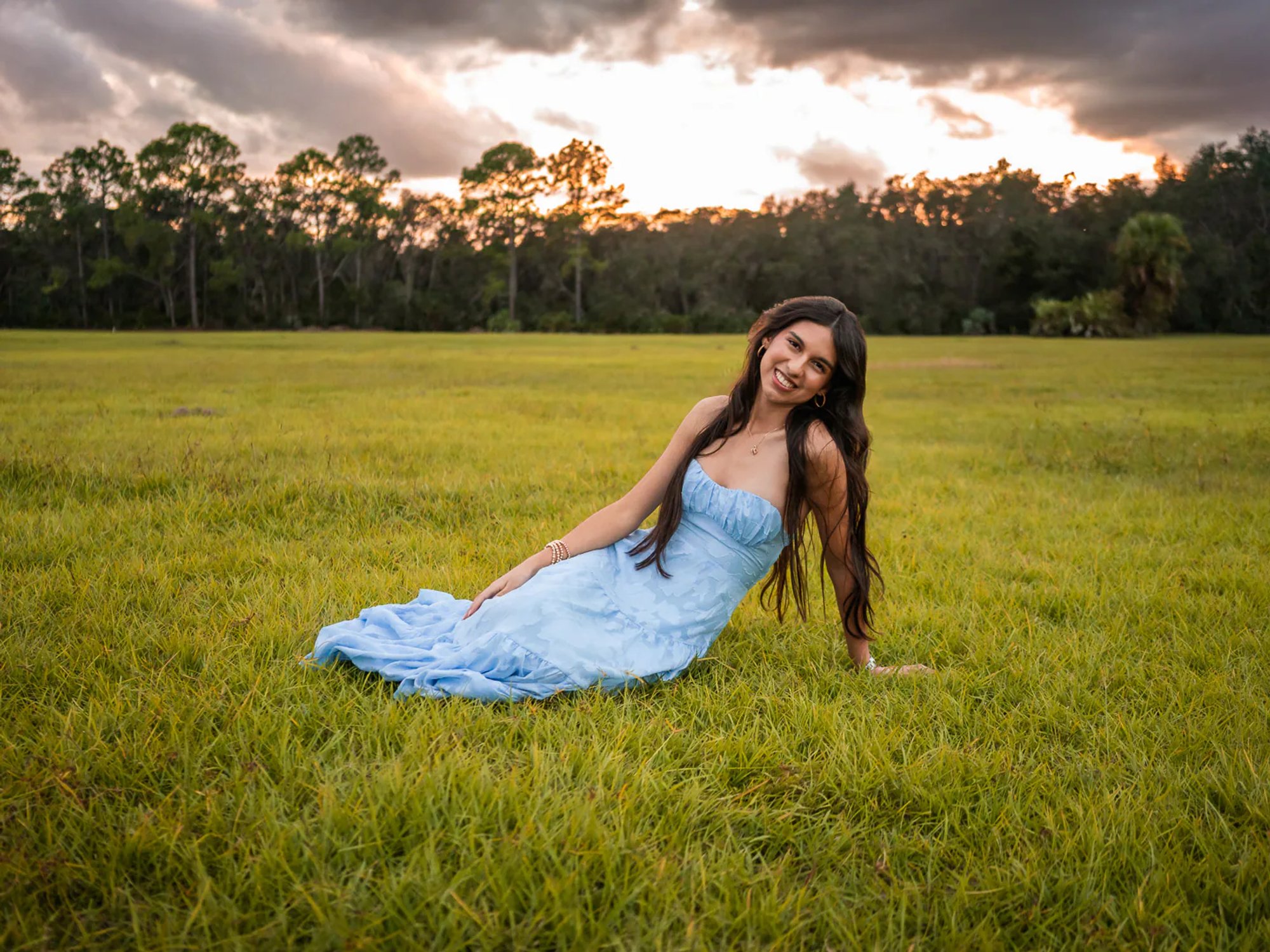 Young woman in a pale blue dress seated on the grass.