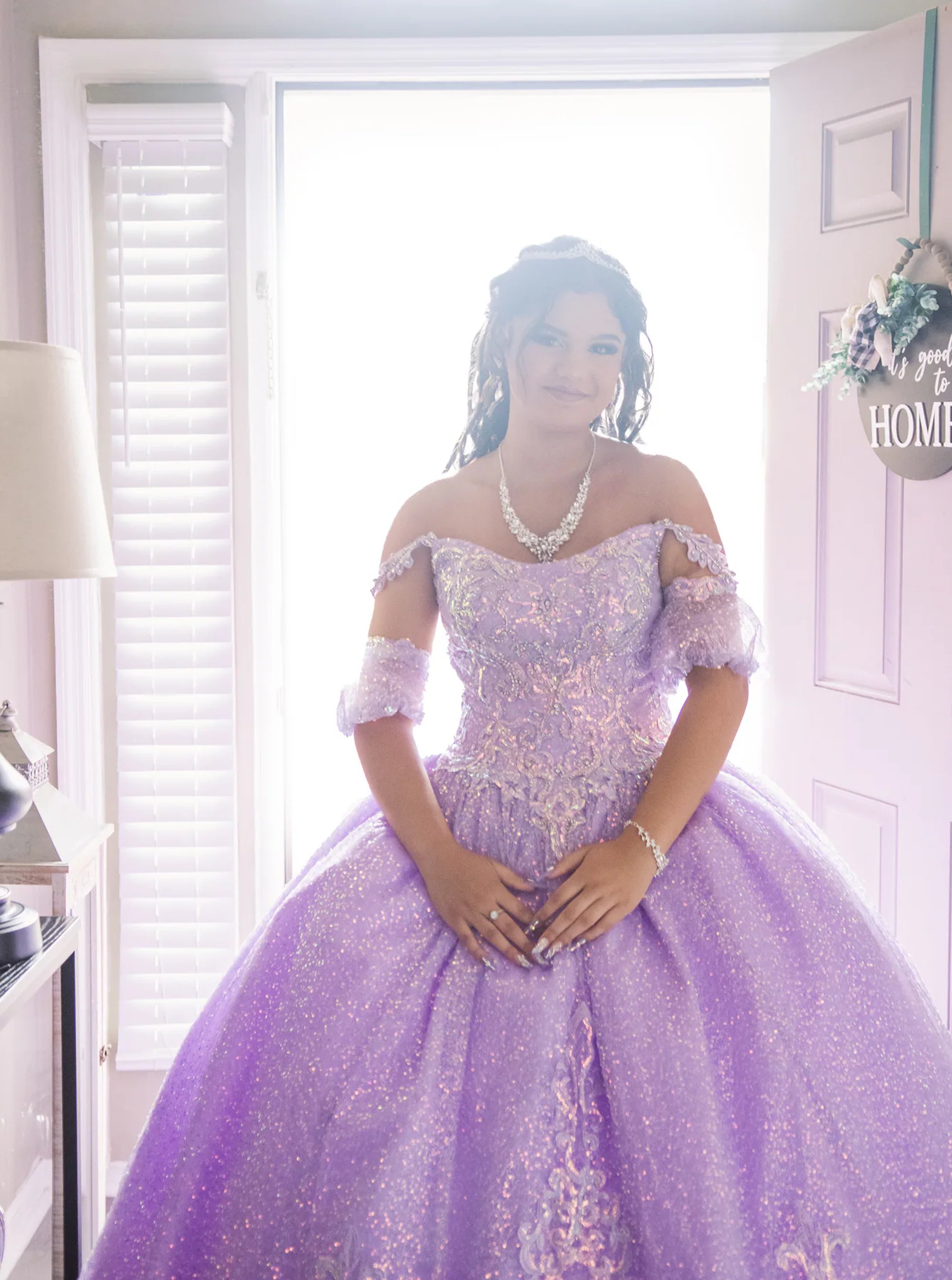 Quinceañera standing in a bright doorway in her purple gown.