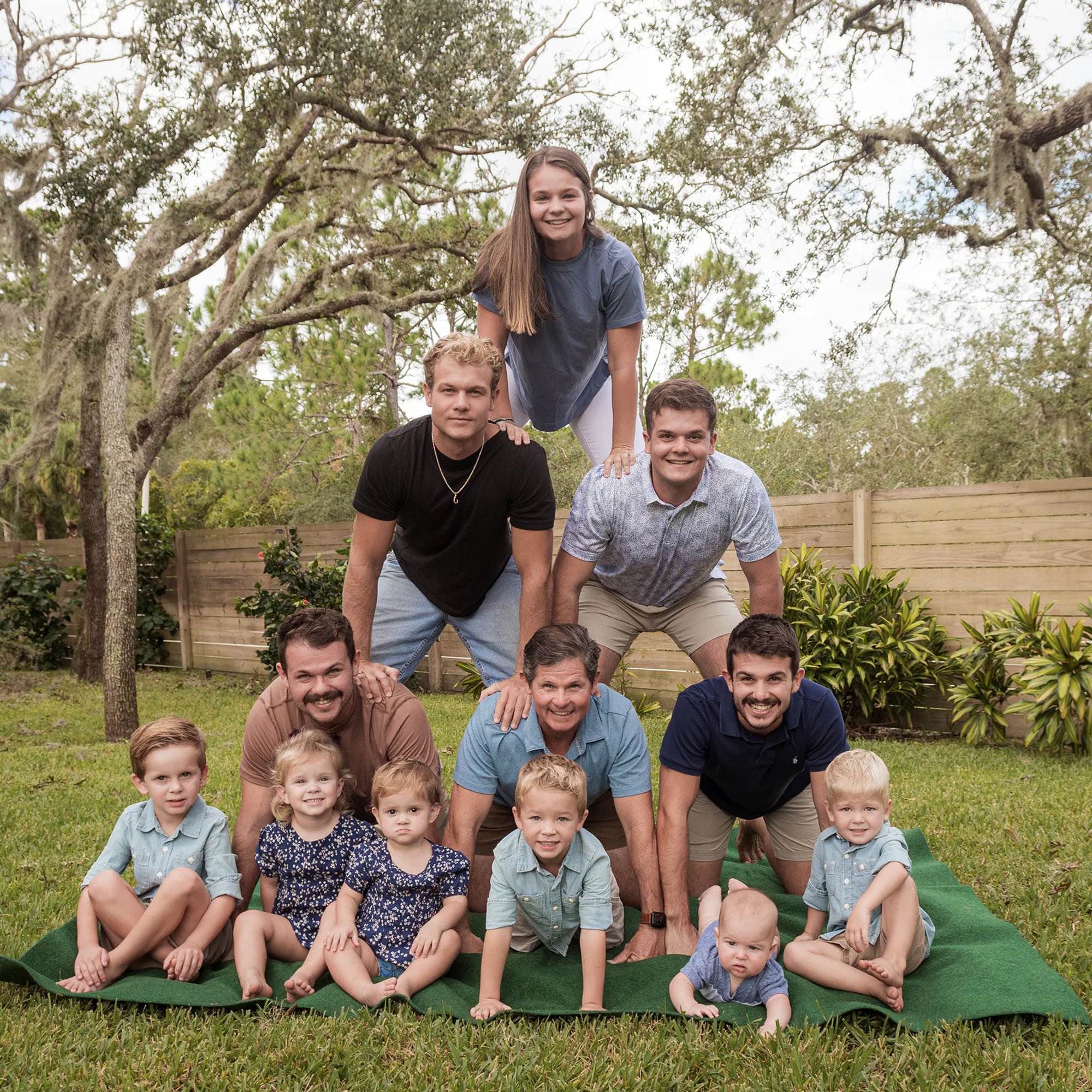 Adults and children forming a playful family pyramid on the grass.