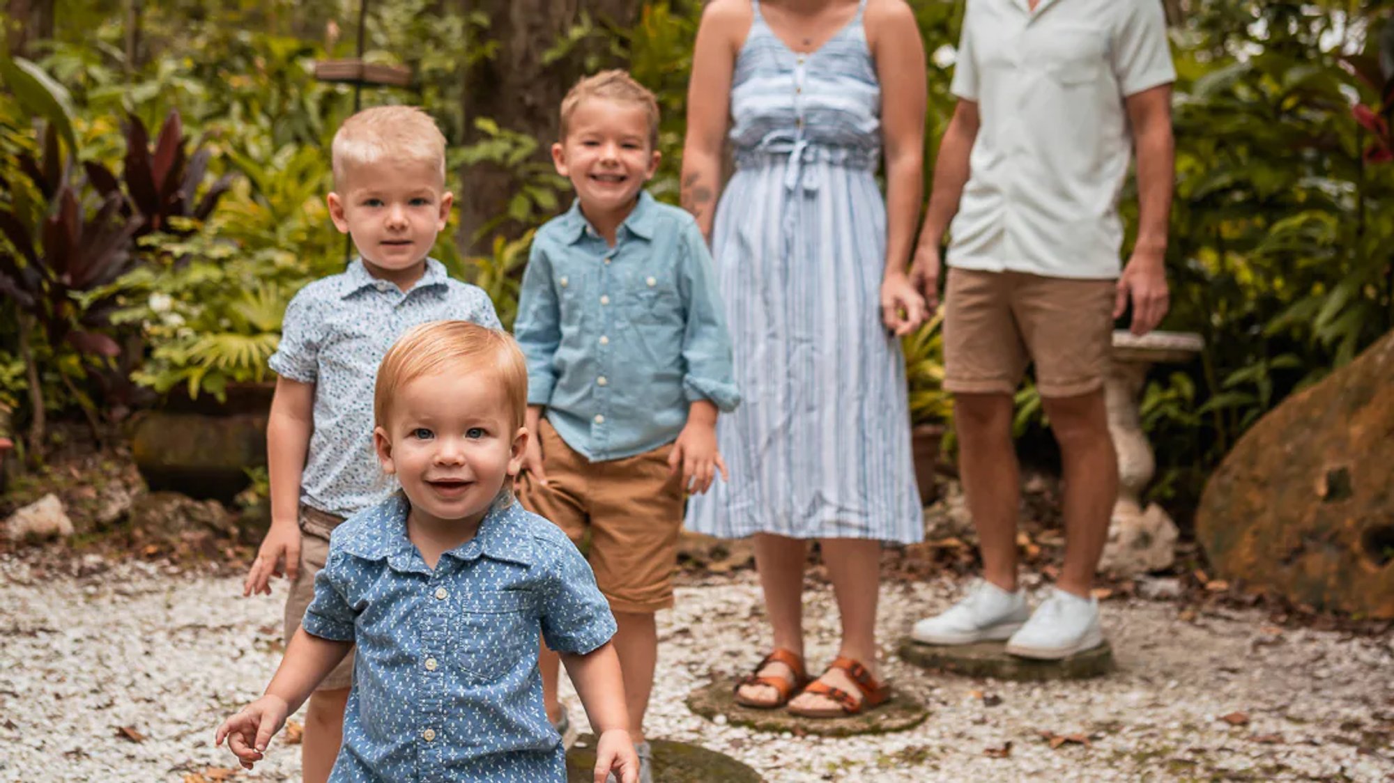Family with three young children gathered together in a tropical garden.