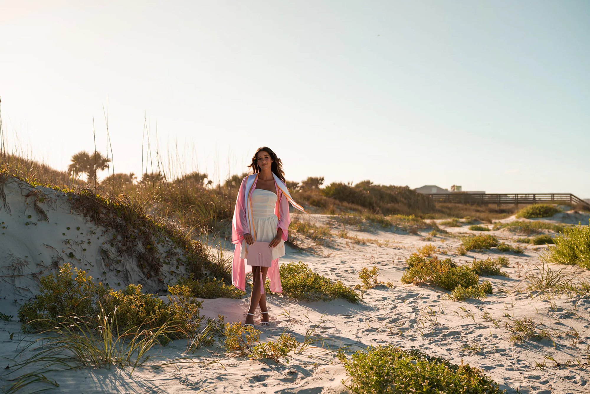 Young woman in a pink wrap standing on a sandy path through the dunes.