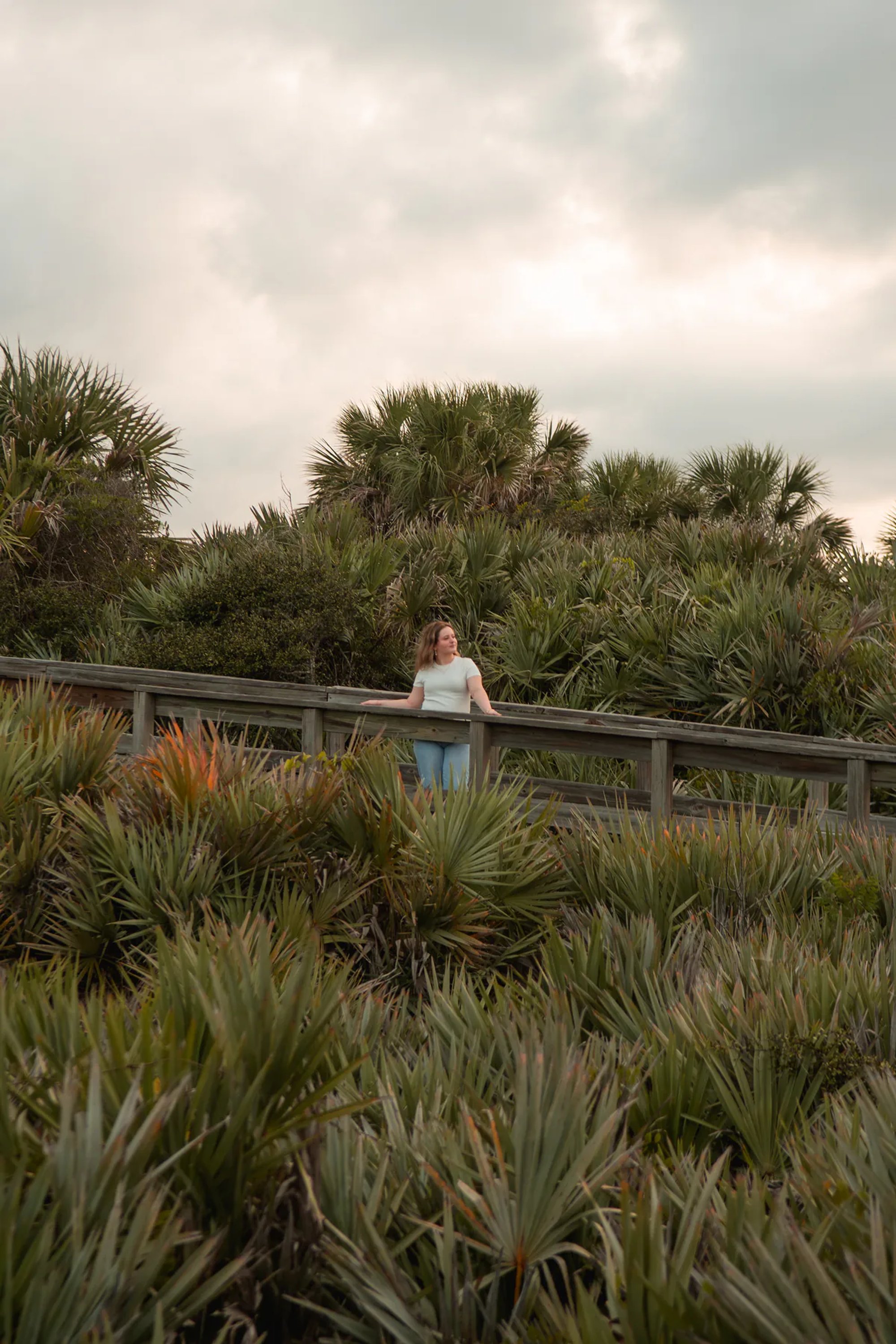 Senior portrait at Ponce Inlet, Nelly smiling while seated on dune with jeans and white shirt during golden hour.