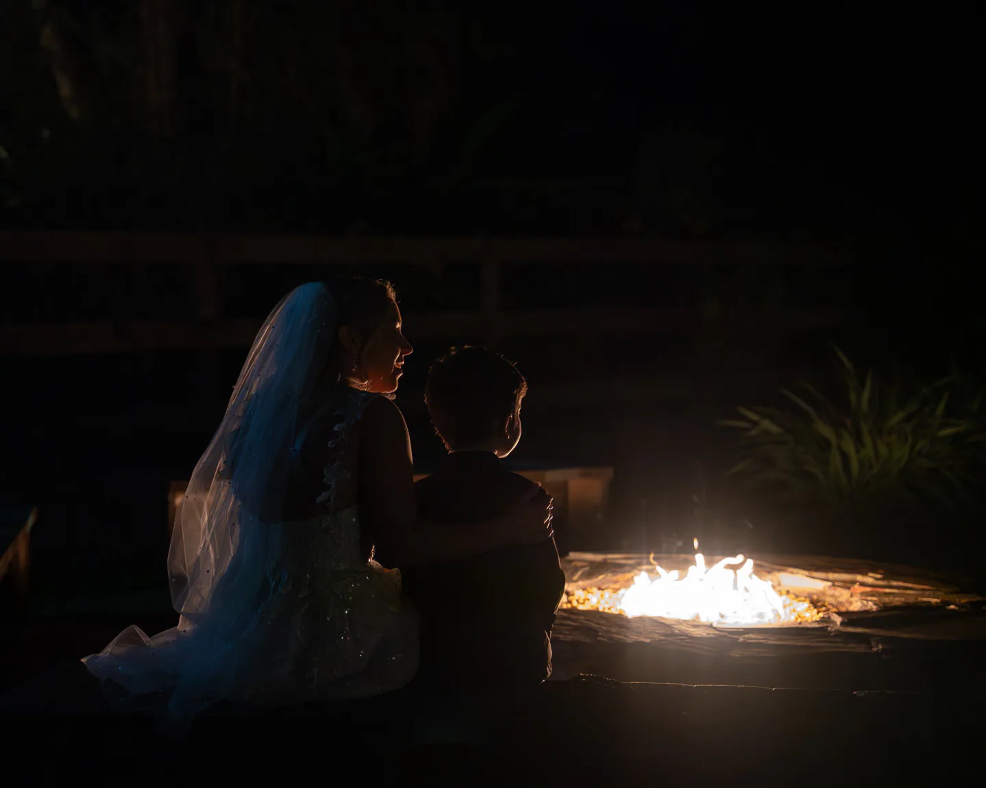 Bride and son sitting by fire pit at night during Bridle Oaks Barn wedding