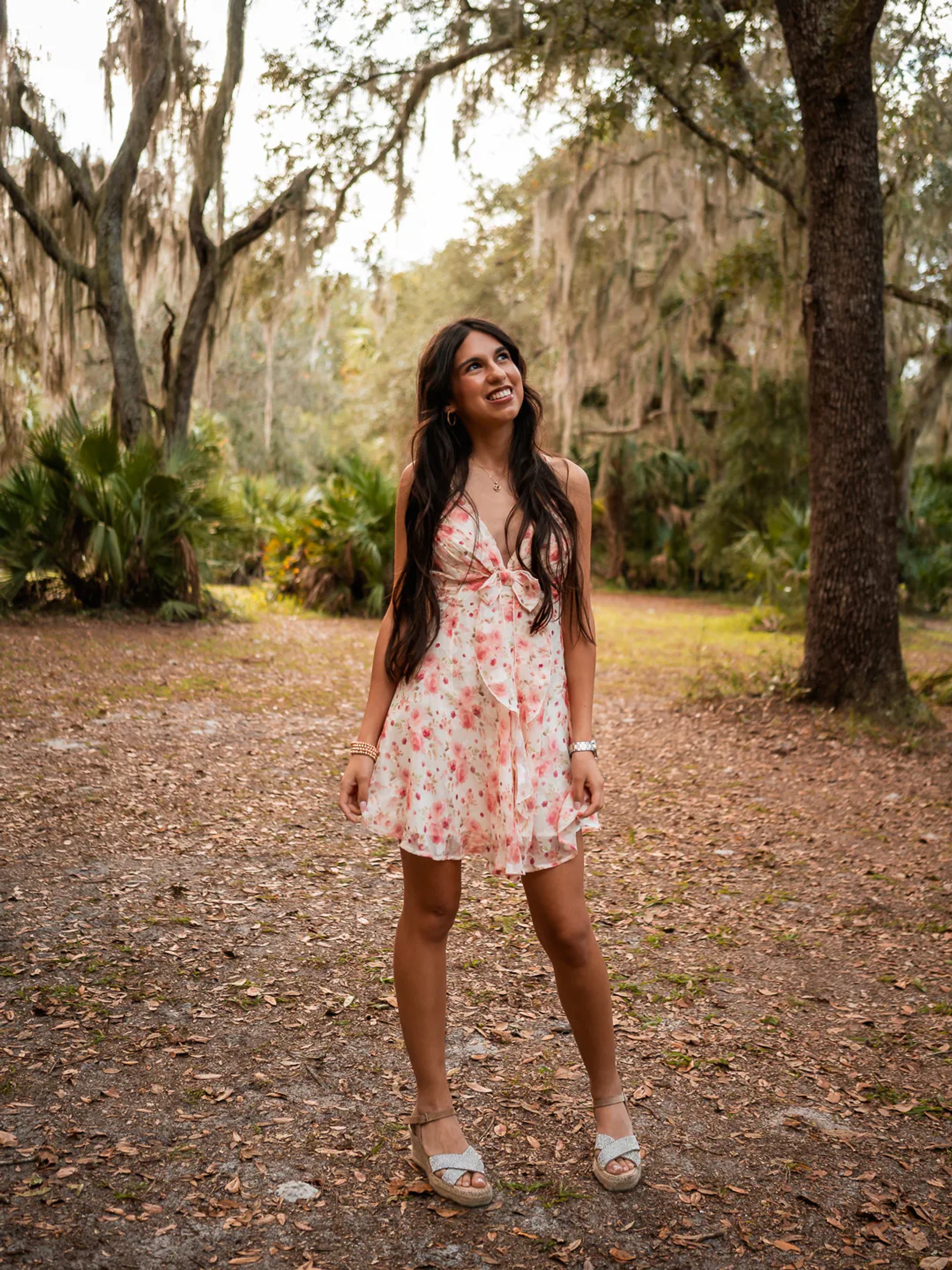 Young woman in a floral dress beneath trees draped with Spanish moss.