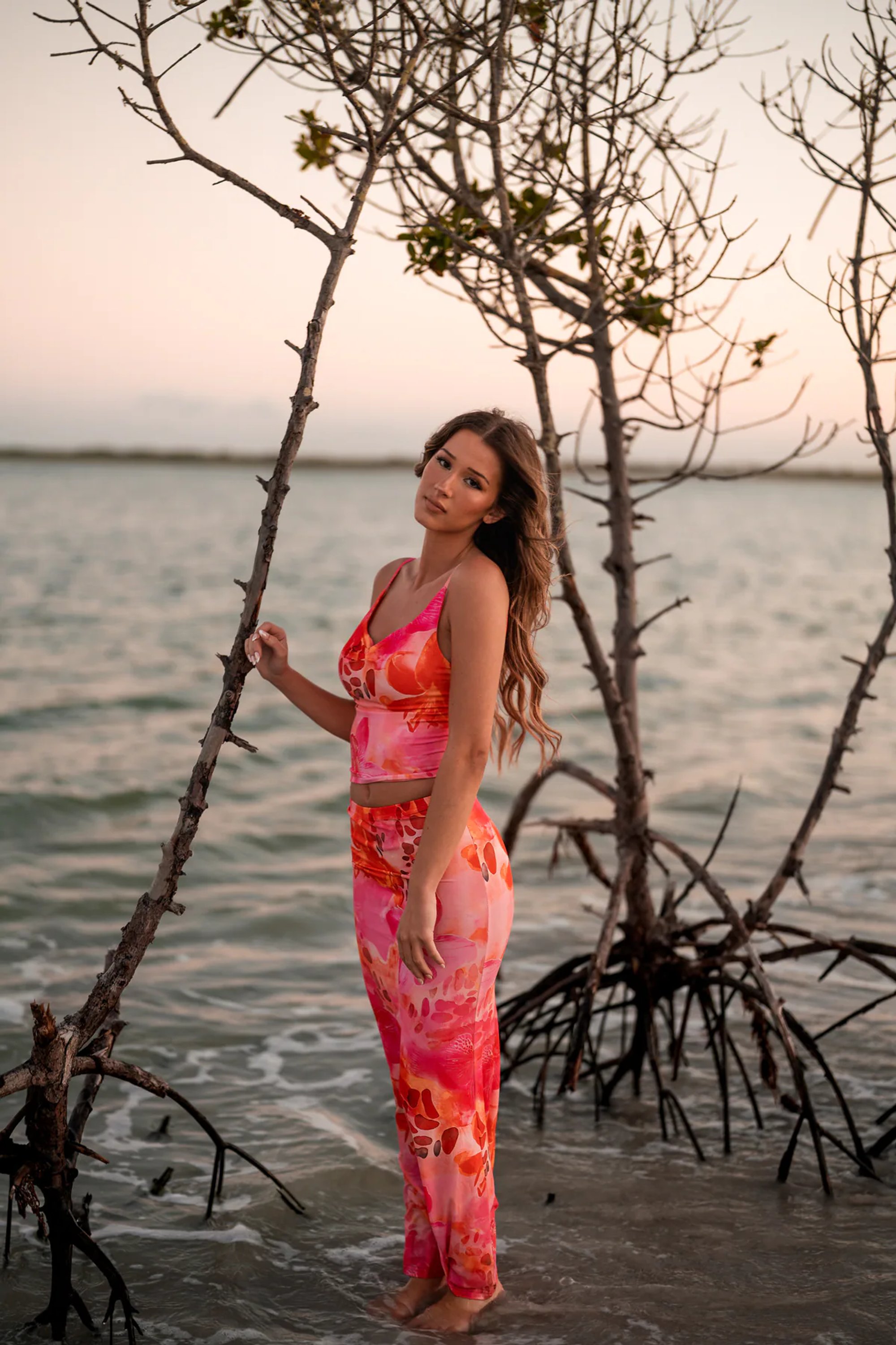 Young woman in a coral patterned dress holding a slender shoreline branch.