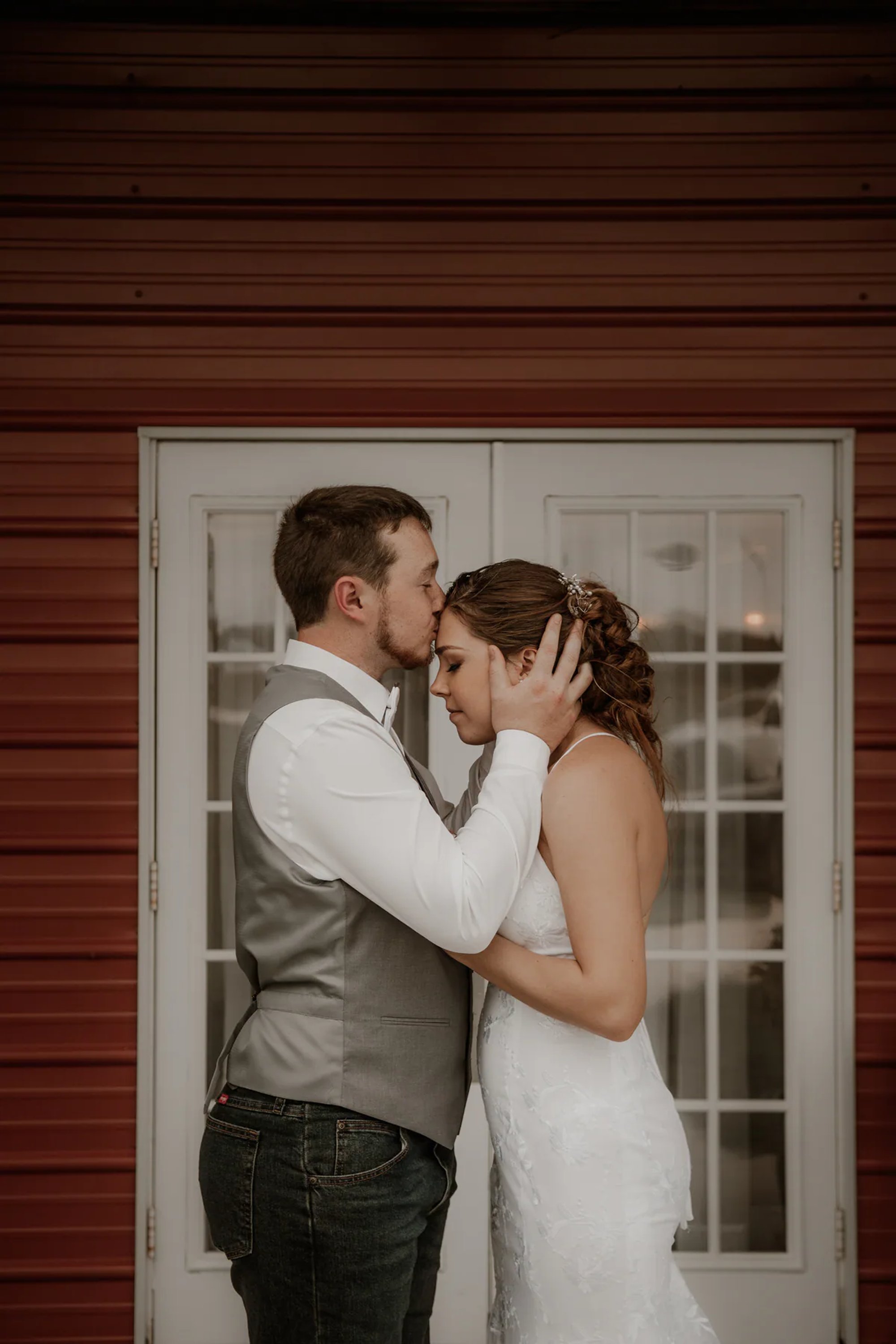 Newlyweds touching foreheads outside a red building.